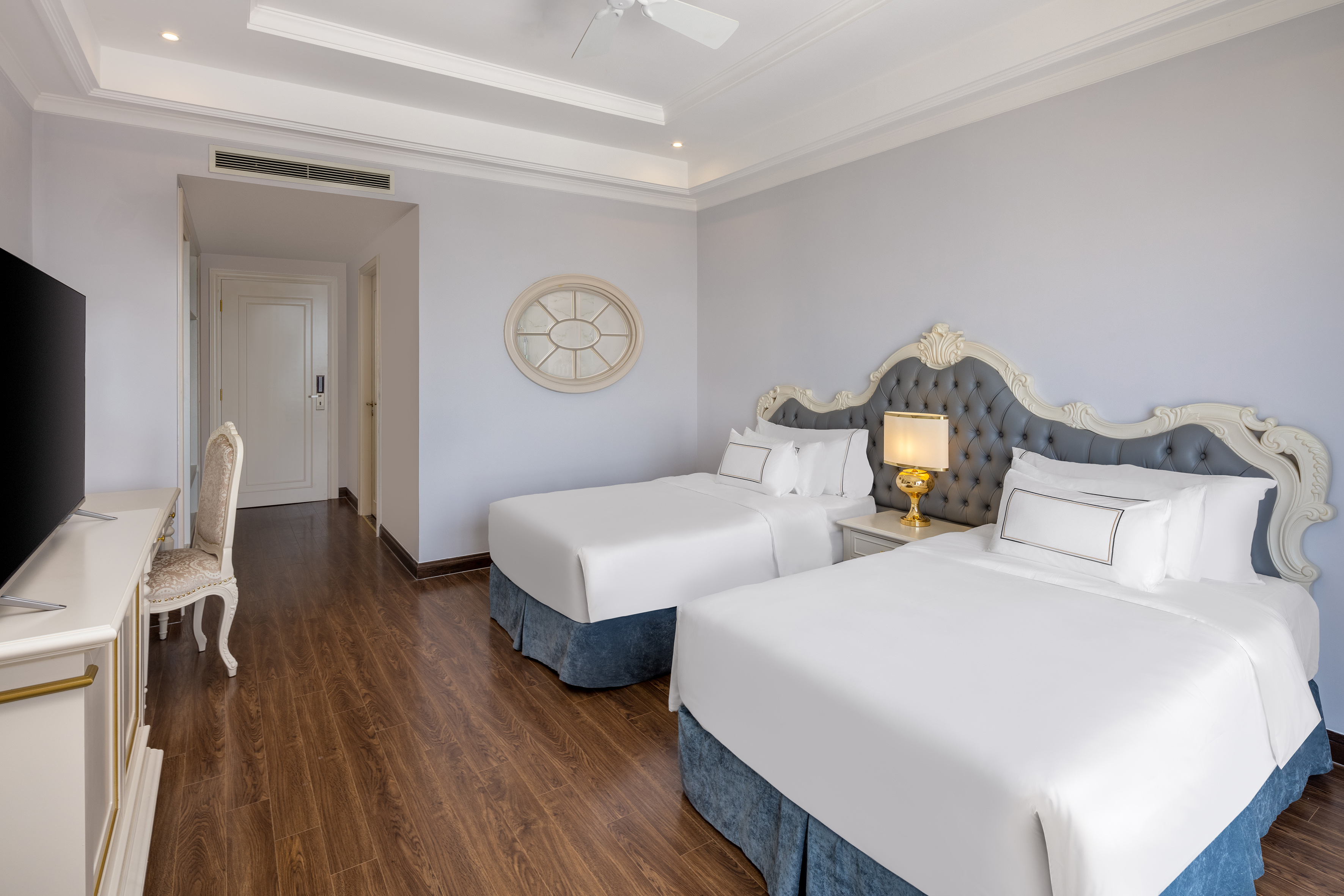 Luxury hotel twin bedroom with ornate headboards, white bedding, and wood floor.