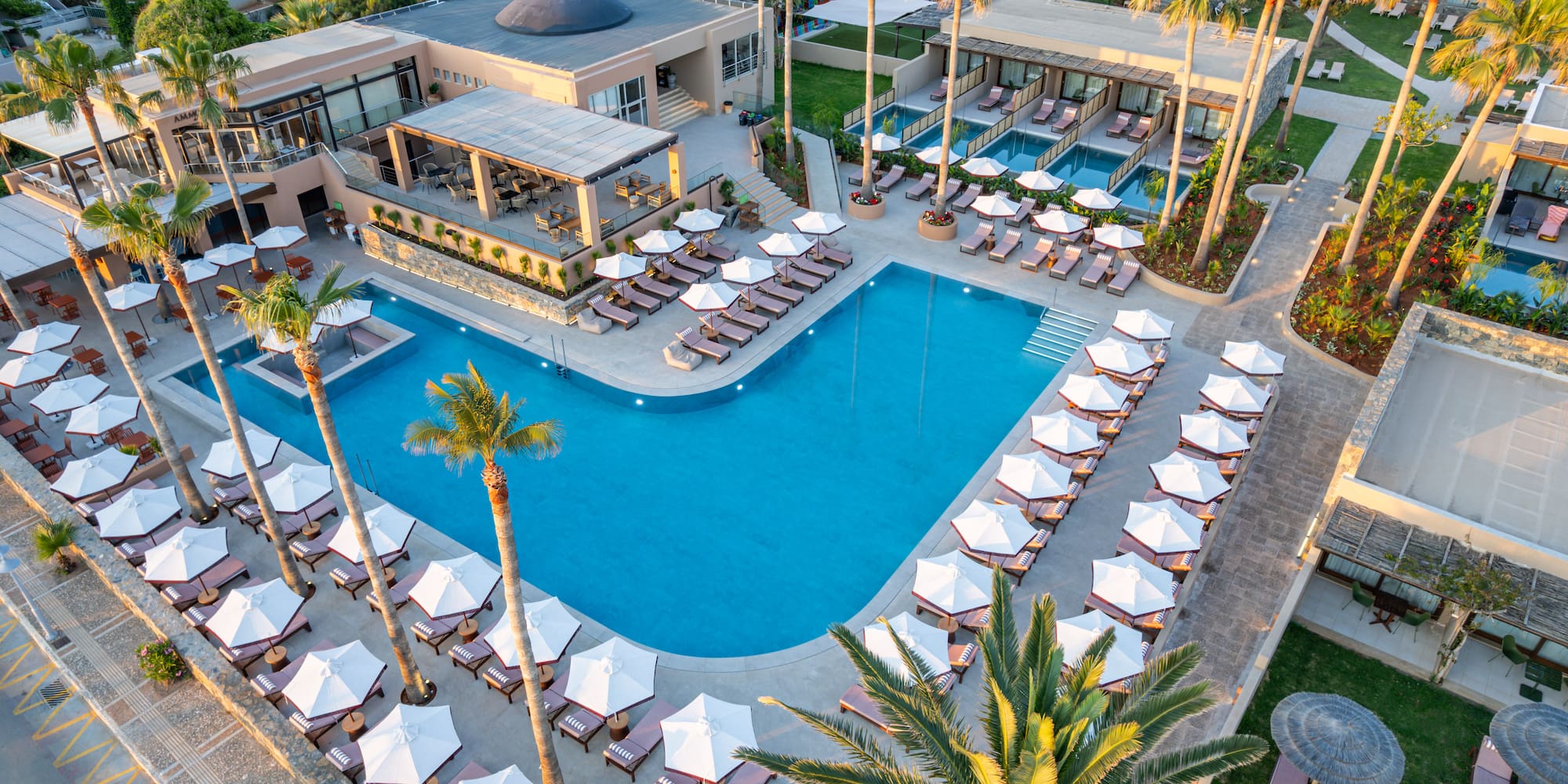 Luxury resort with large swimming pool, sunbeds, and palm trees.