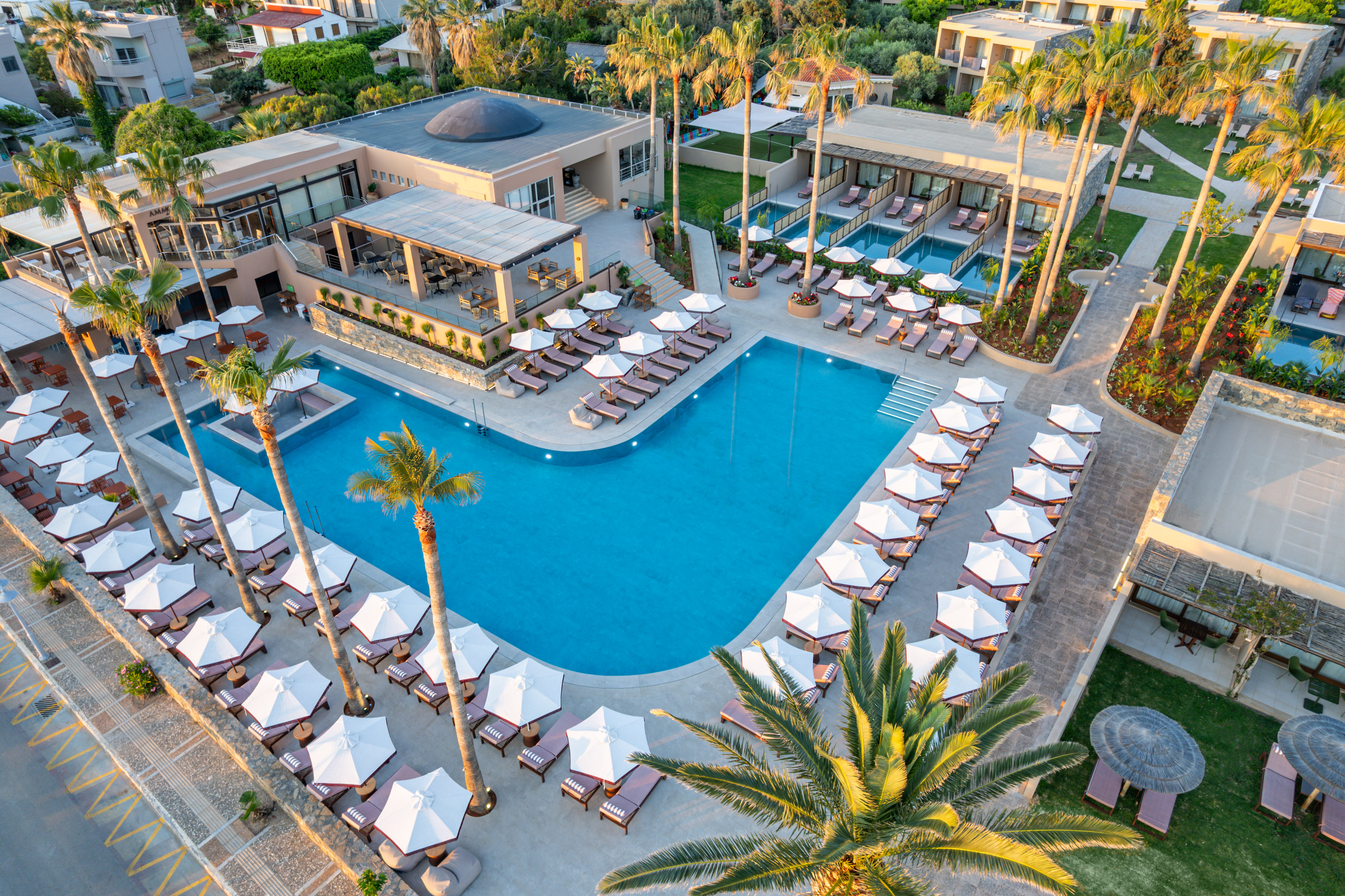 Luxury resort with large swimming pool, sunbeds, and palm trees.