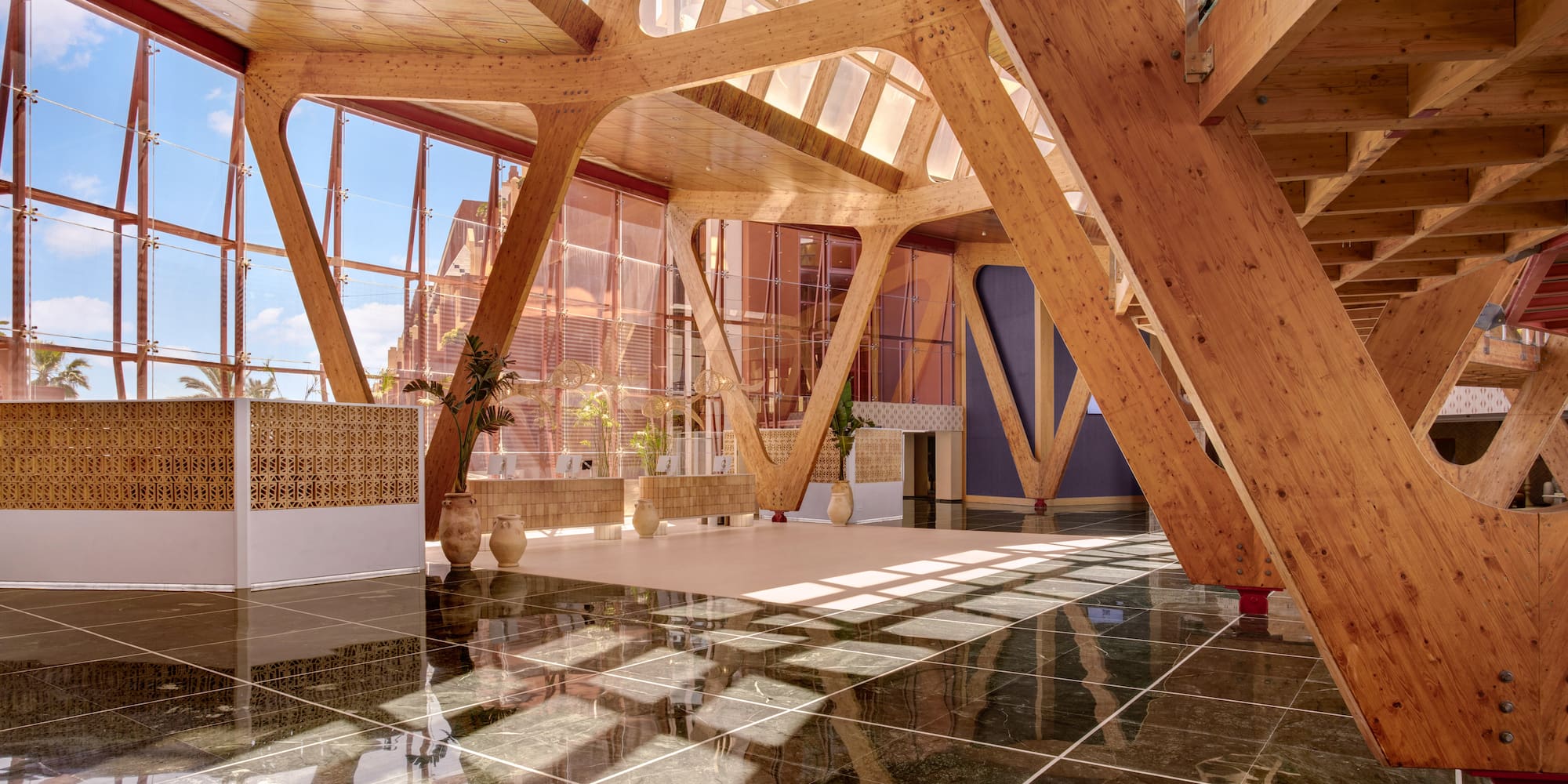 Grand atrium with exposed wooden beams, glass walls, and glossy marble floor.