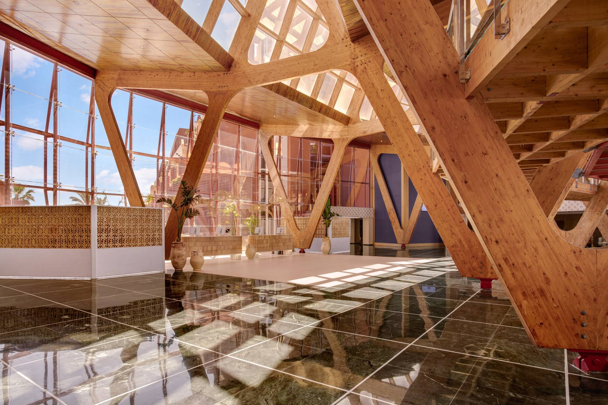 Grand atrium with exposed wooden beams, glass walls, and glossy marble floor.