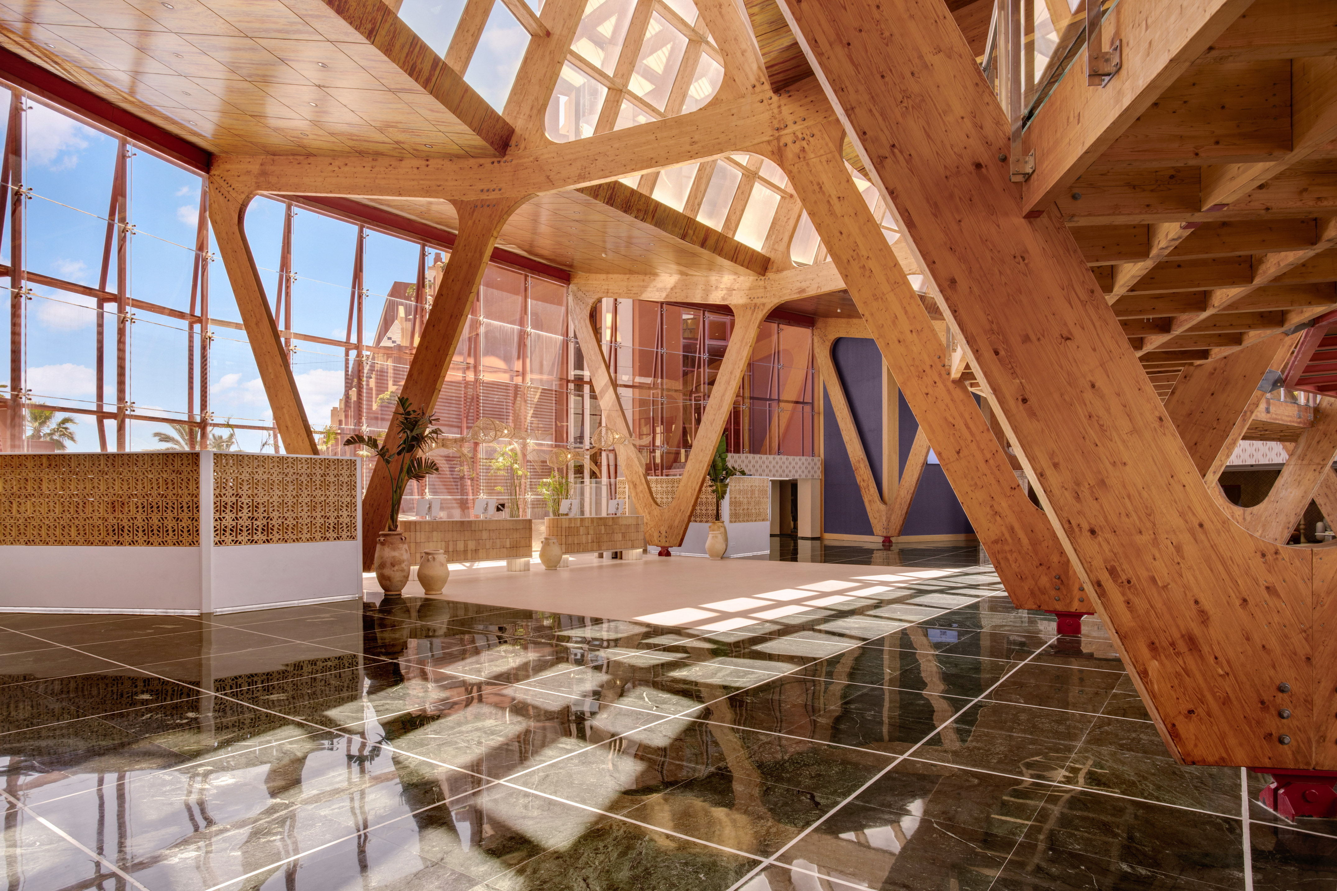 Grand atrium with exposed wooden beams, glass walls, and glossy marble floor.