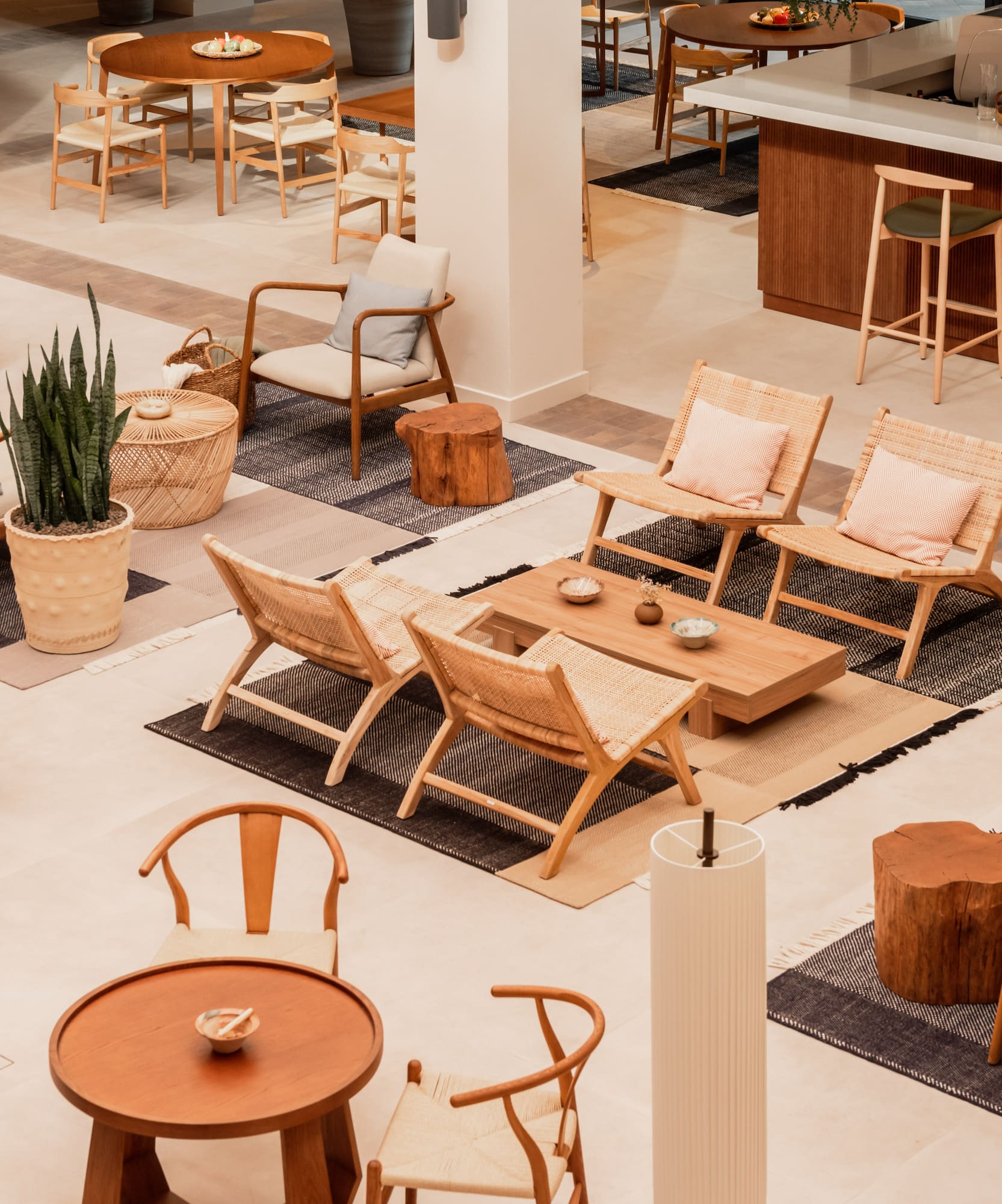 Hotel lobby lounge with modern wood and rattan furniture, bar, and area rugs.