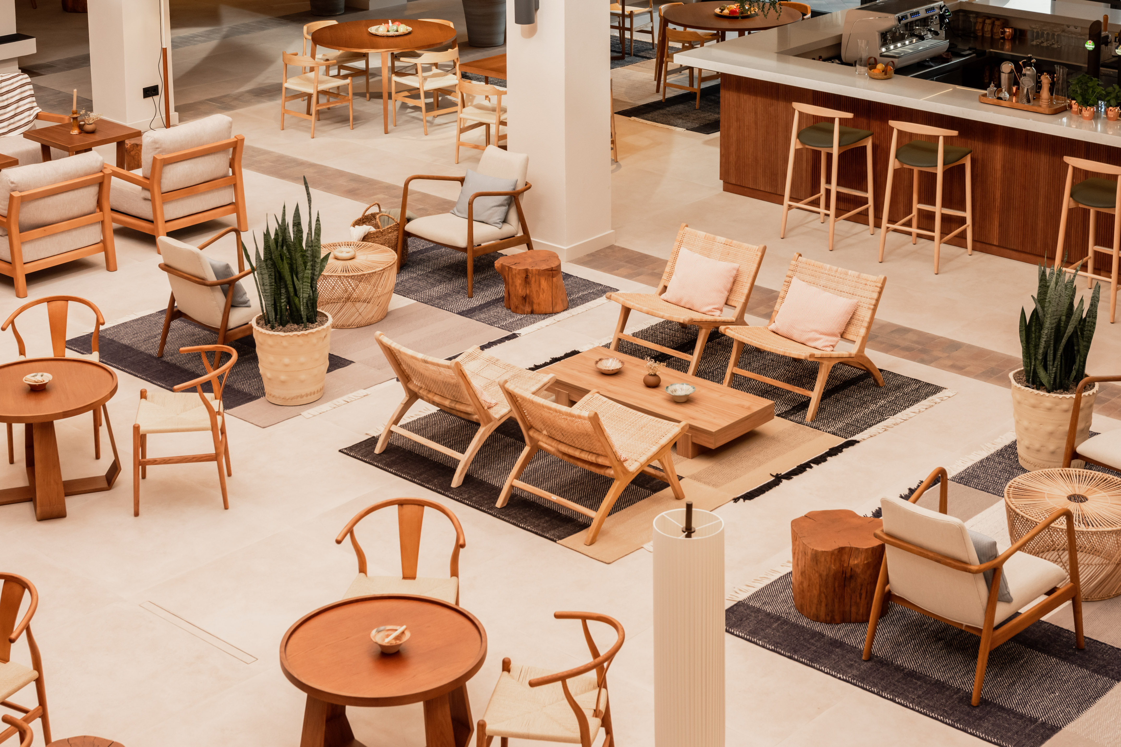 Hotel lobby lounge with modern wood and rattan furniture, bar, and area rugs.