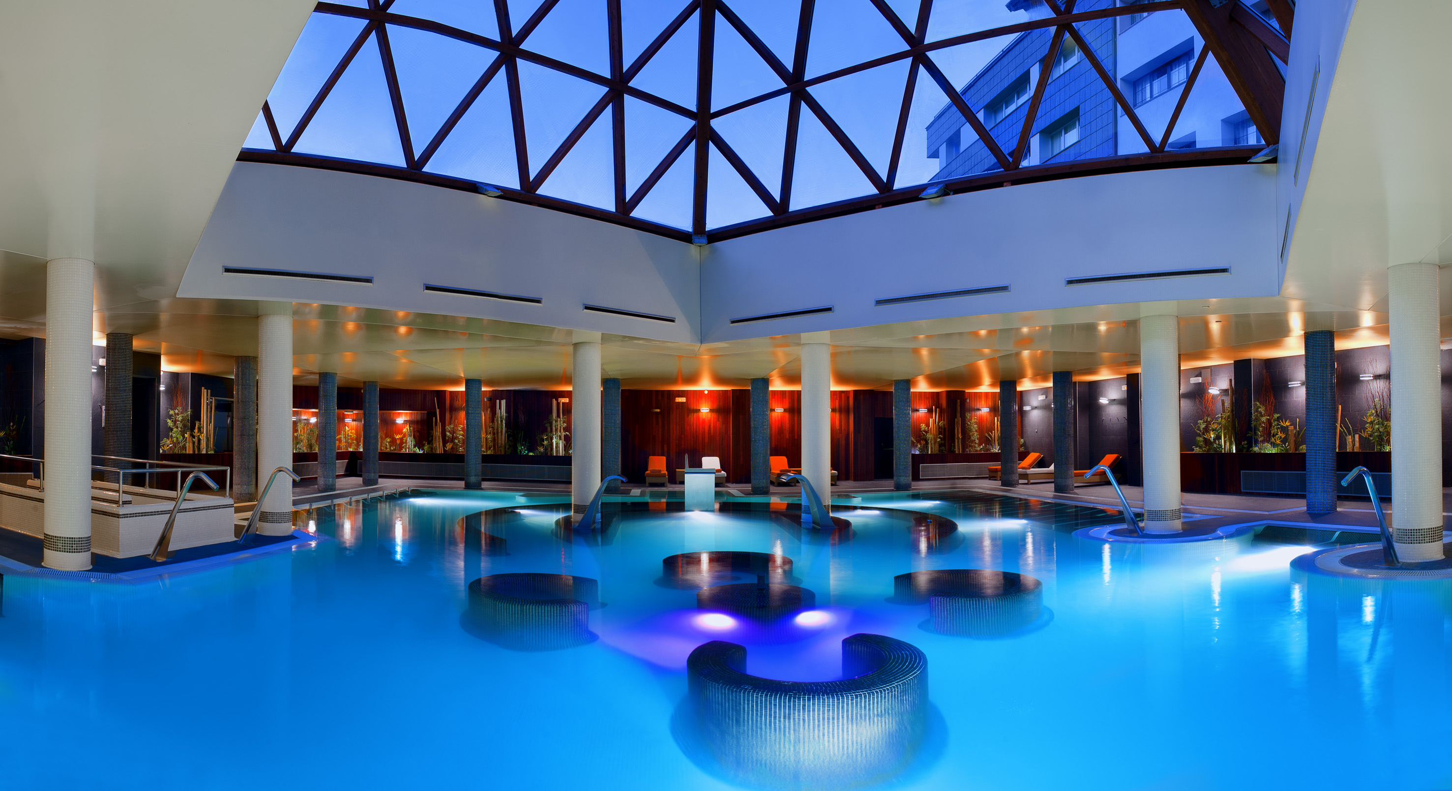 Indoor spa pool with blue water, overhead skylight, and warm accent lighting.