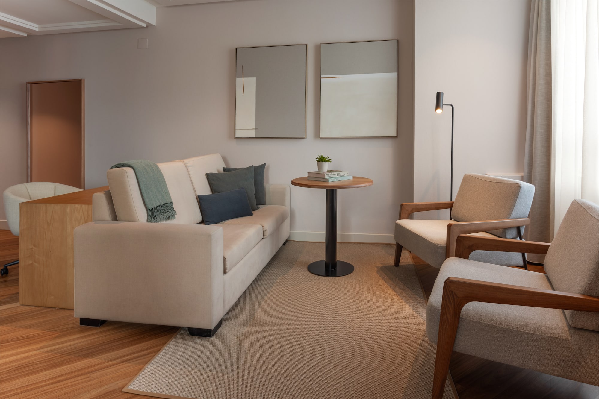 Salón moderno con sofá claro, dos sillones, alfombra y arte de pared.