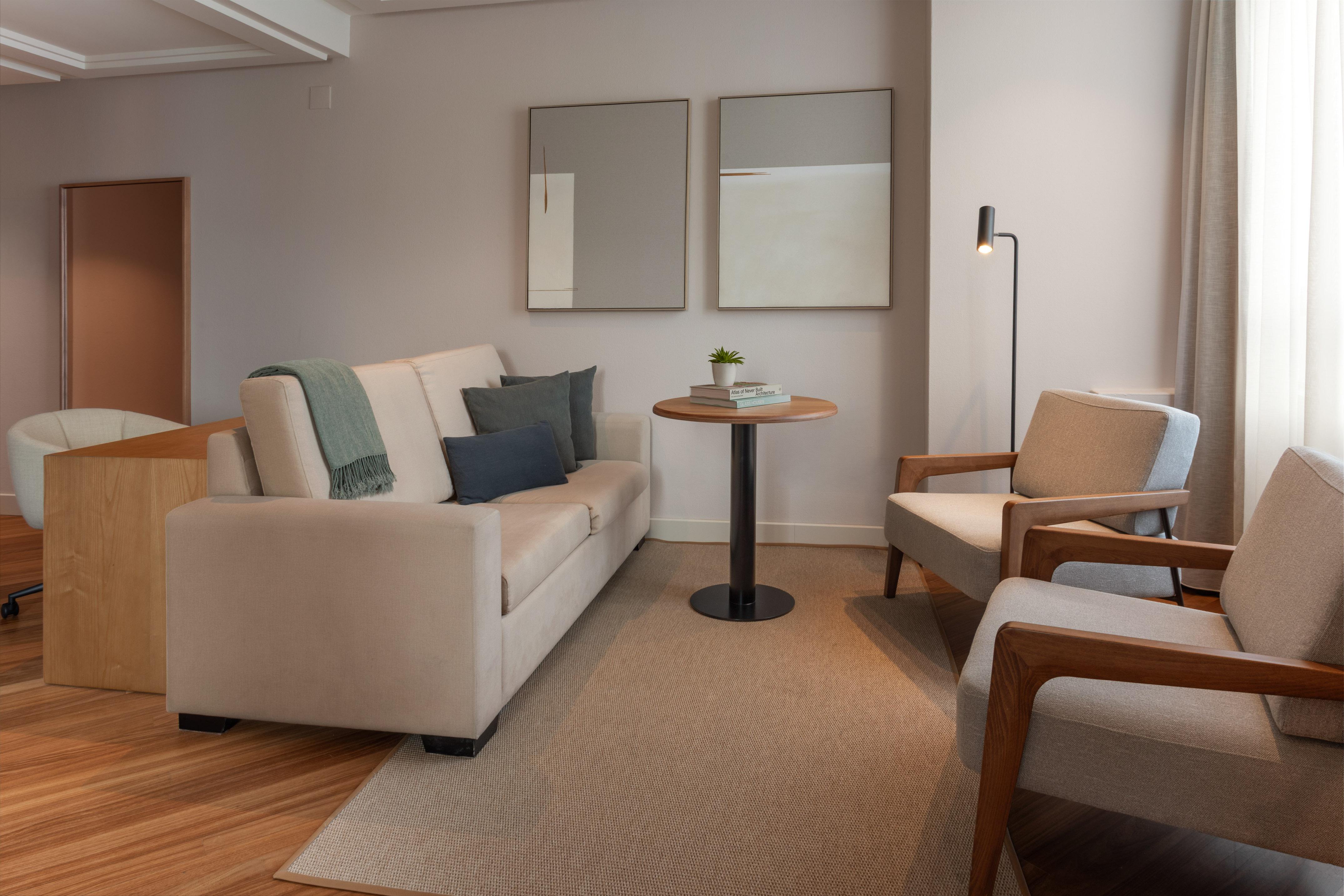 Salón moderno con sofá claro, dos sillones, alfombra y arte de pared.