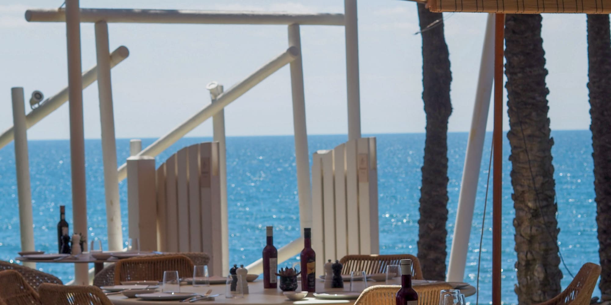 Seaside restaurant with set tables, rattan chairs, and sparkling blue ocean.