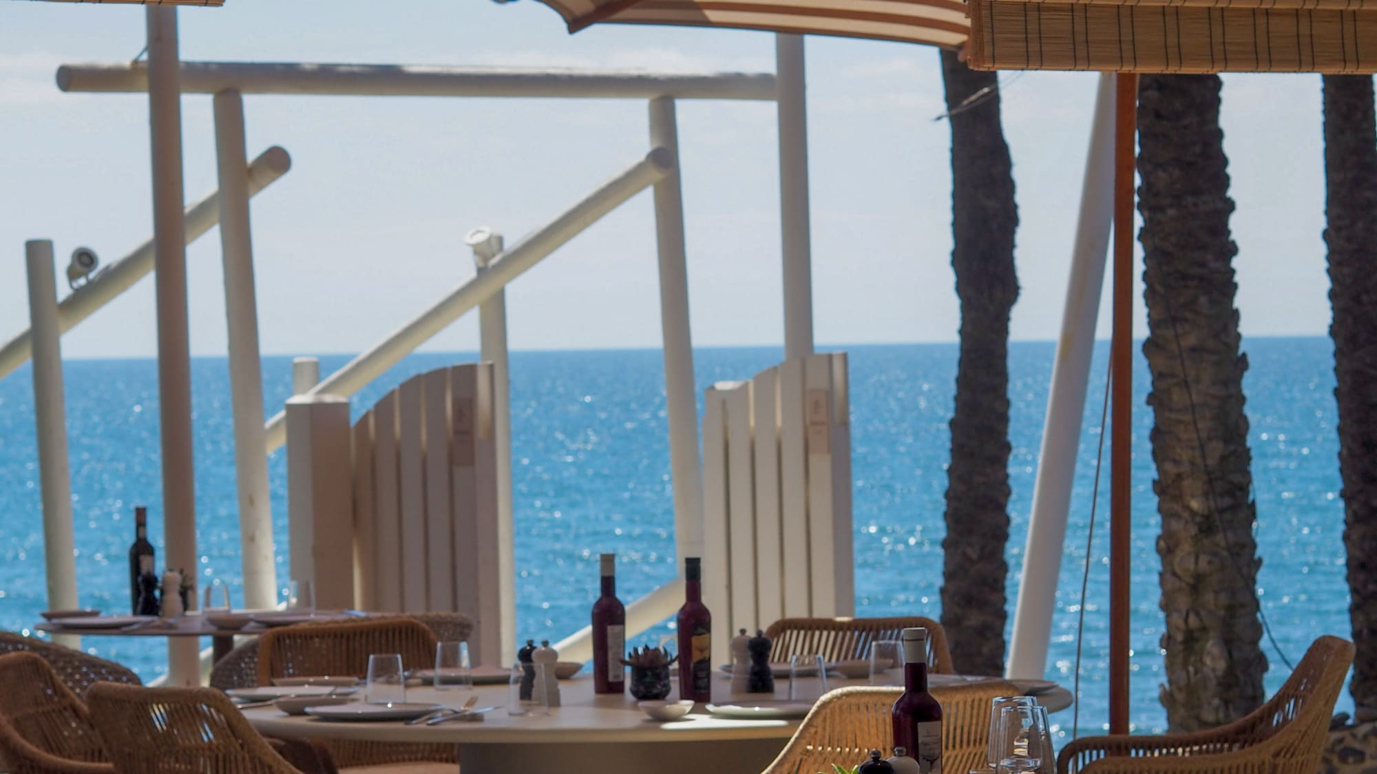 Seaside restaurant with set tables, rattan chairs, and sparkling blue ocean.