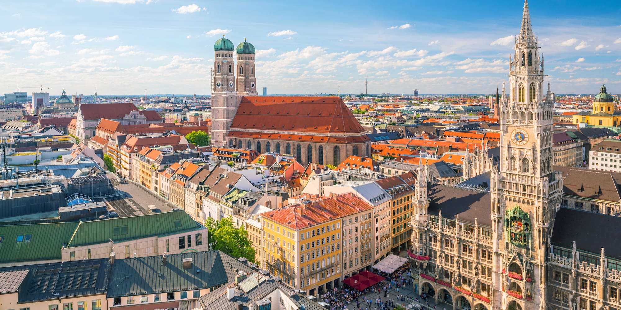 Munich cityscape: Frauenkirche, New Town Hall, and bustling Marienplatz under blue sky.