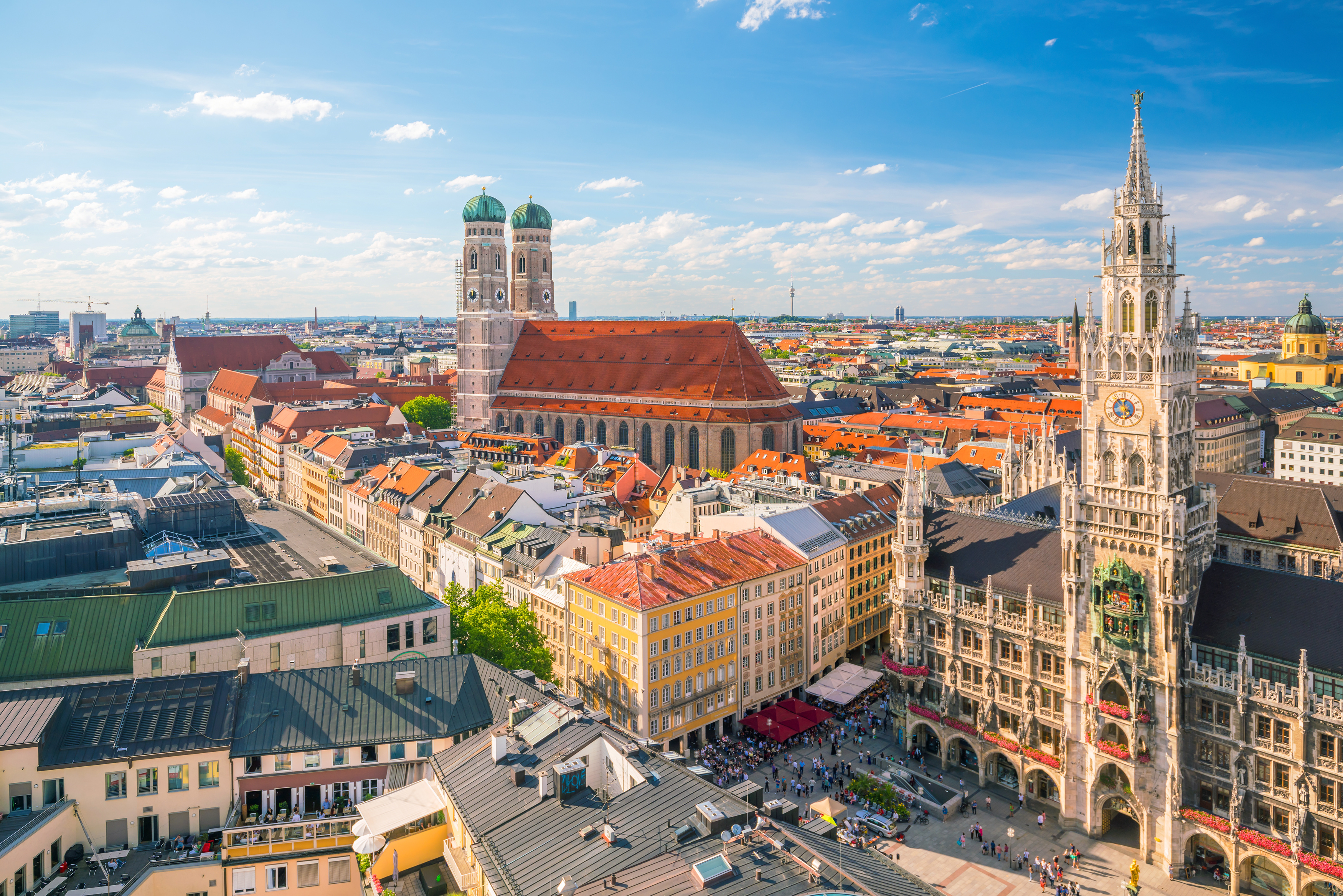 Munich cityscape: Frauenkirche, New Town Hall, and bustling Marienplatz under blue sky.