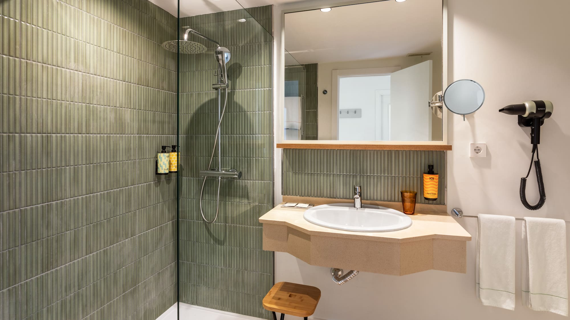 Modern hotel bathroom with green tiled shower, vanity, sink, and mirror.