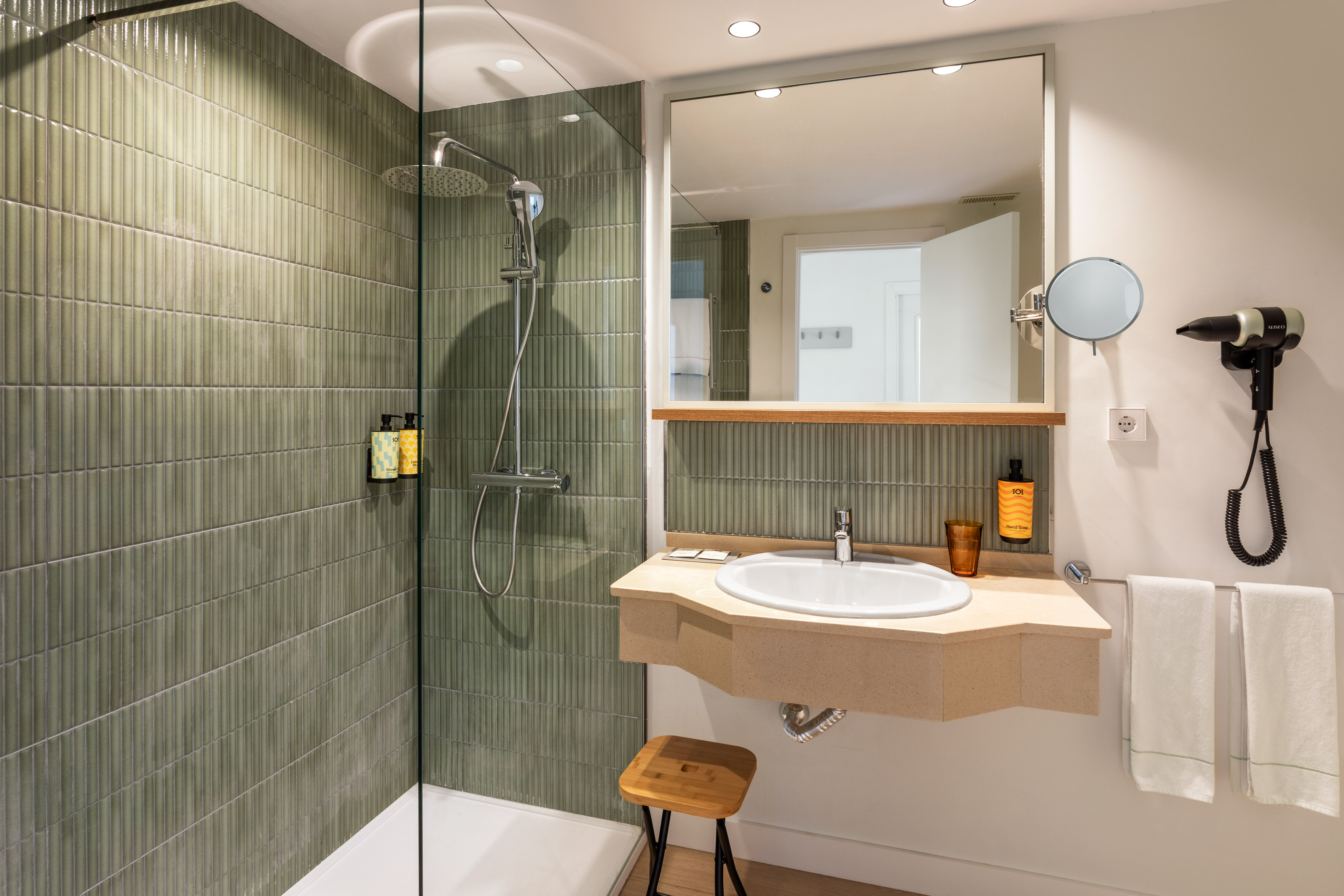 Modern hotel bathroom with green tiled shower, vanity, sink, and mirror.