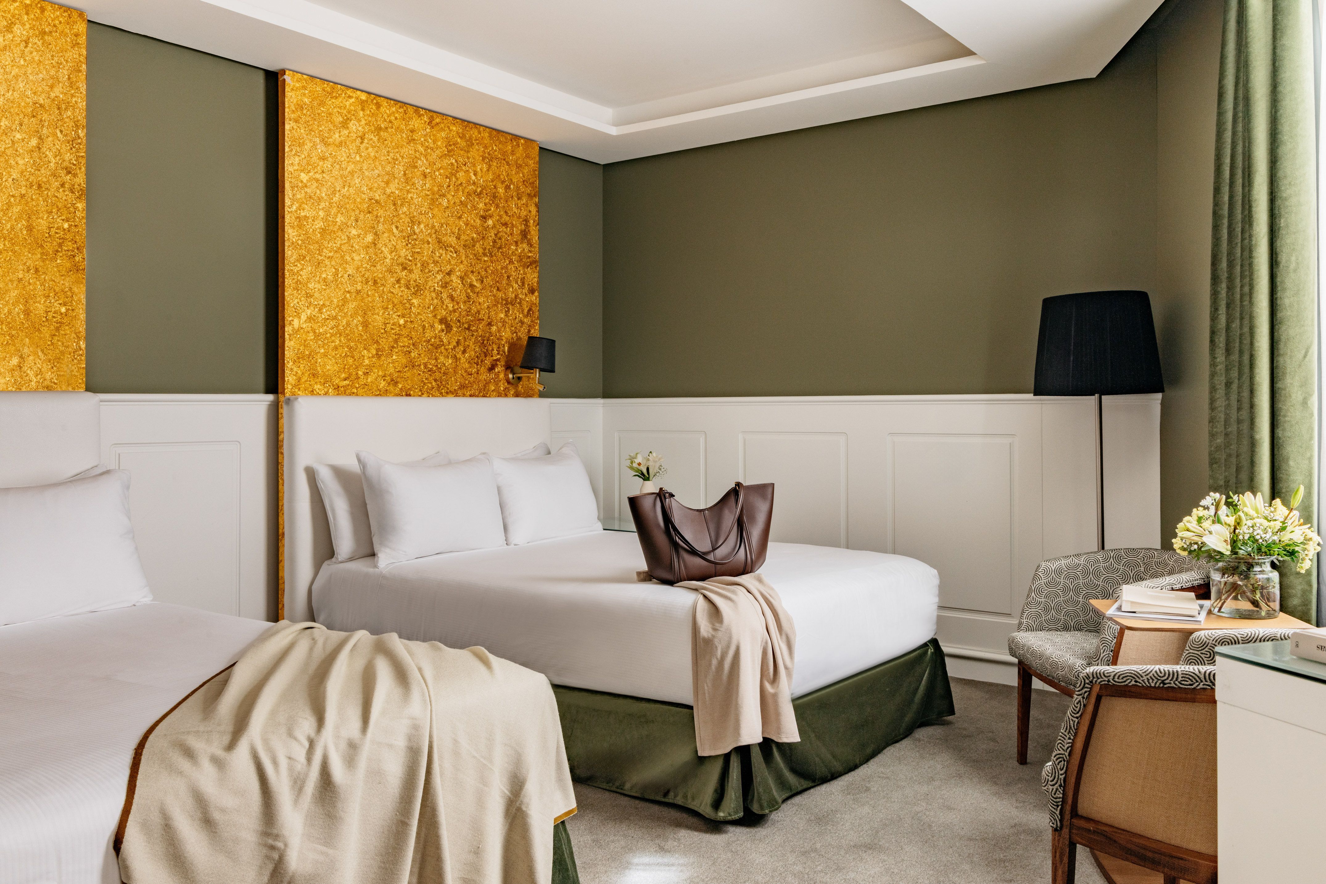 Habitación de hotel con dos camas, decoración en tonos verde oliva y oro.
