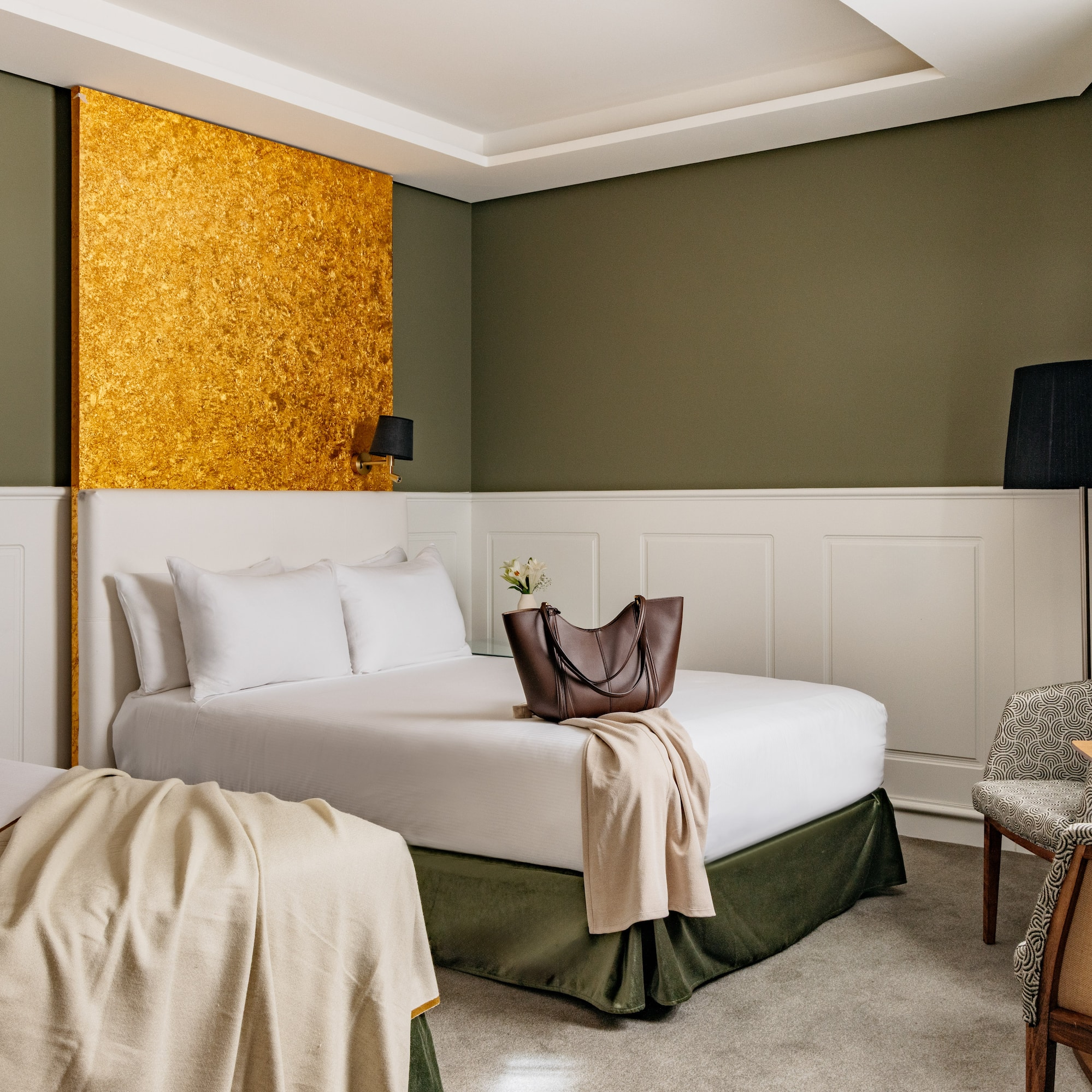 Habitación de hotel con dos camas, decoración en tonos verde oliva y oro.