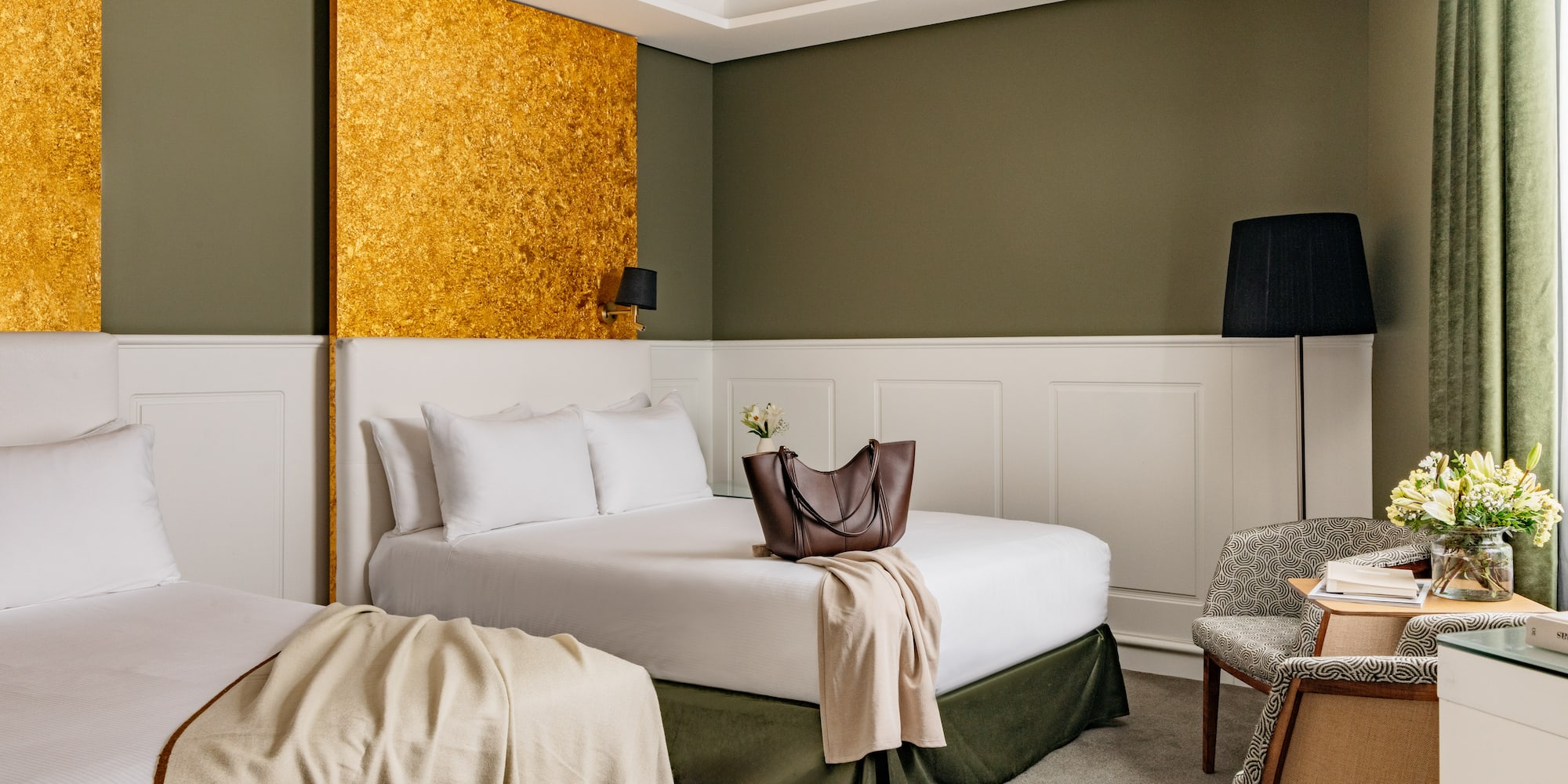 Habitación de hotel con dos camas, decoración en tonos verde oliva y oro.