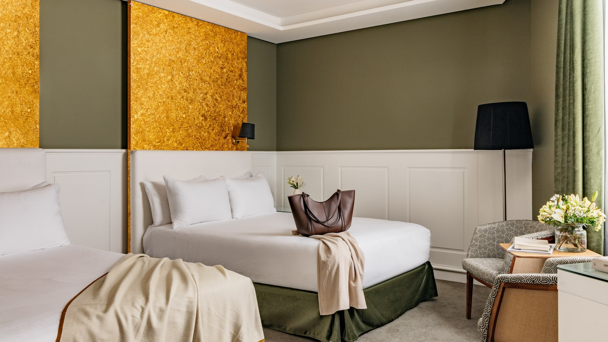 Habitación de hotel con dos camas, decoración en tonos verde oliva y oro.