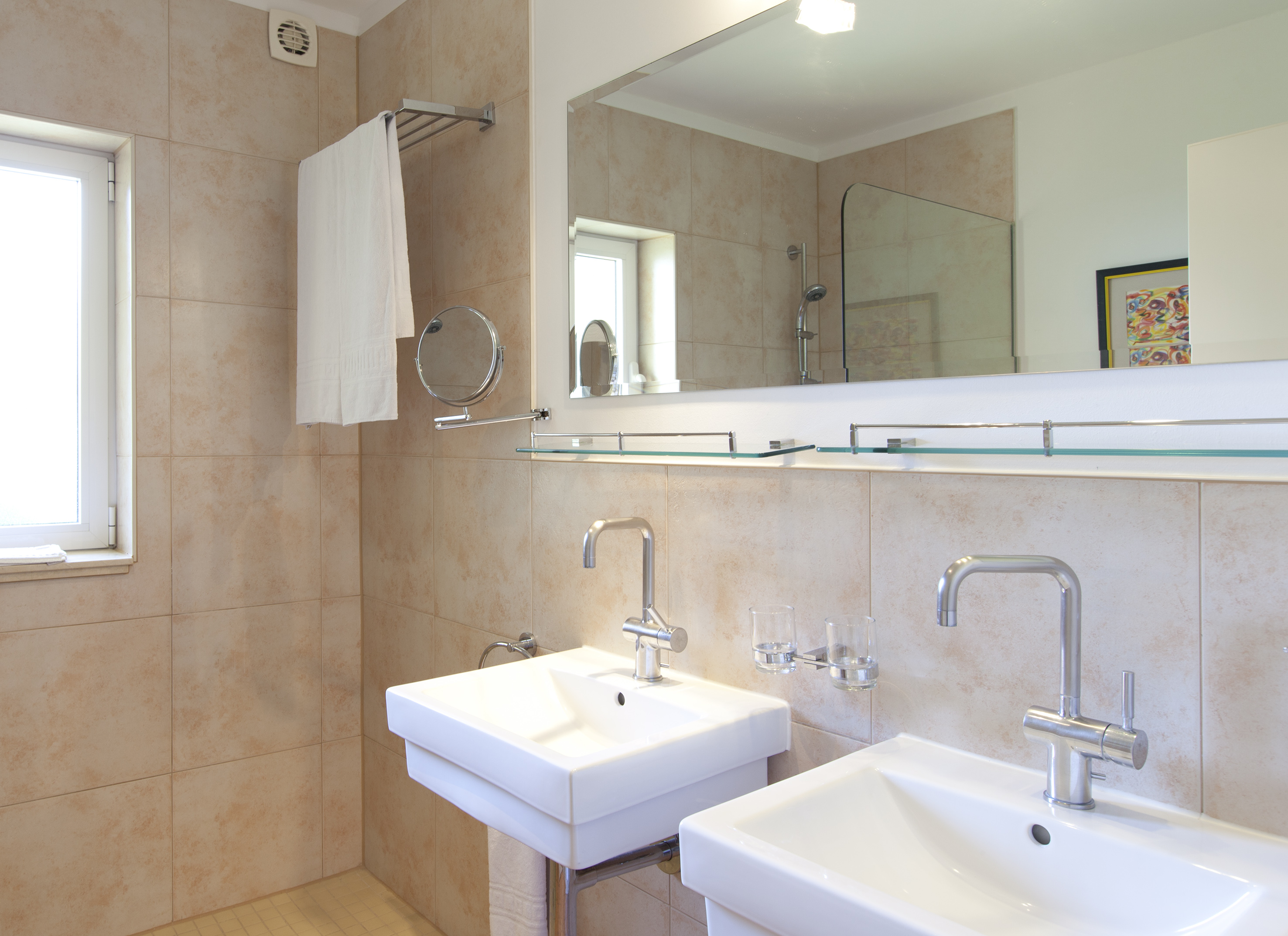 Modern tiled bathroom with double vanity, chrome faucets, mirror, shower.