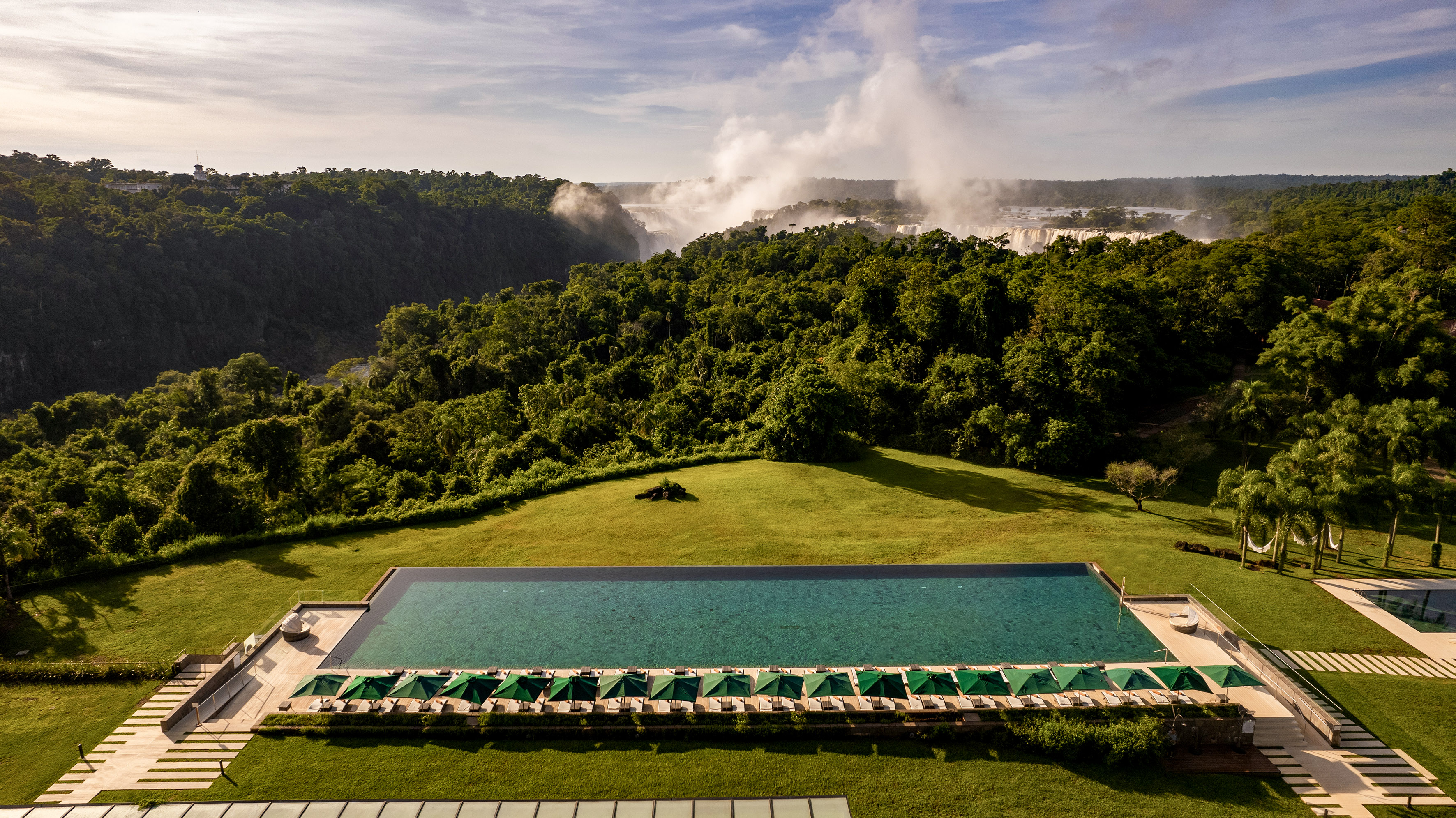 Luxury resort infinity pool with Iguazu Falls and rainforest view.