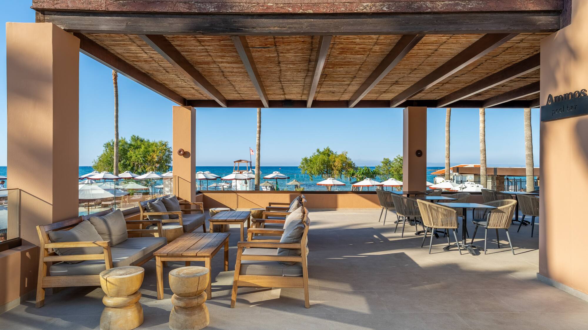 Ammos pool bar terrace with shaded lounge and dining, beach and sea view.
