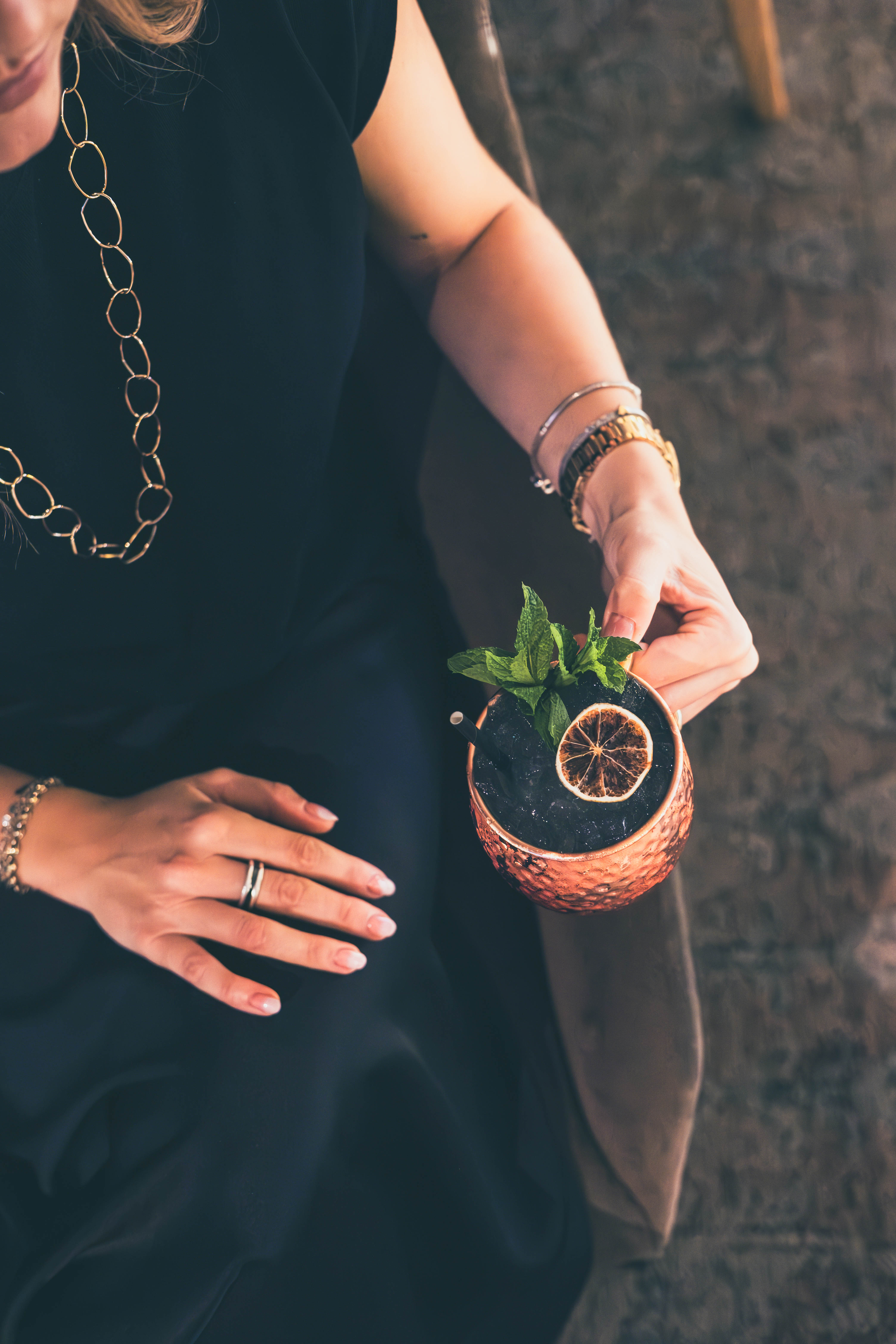 Woman's hands hold copper mug cocktail with mint, dried orange slice.
