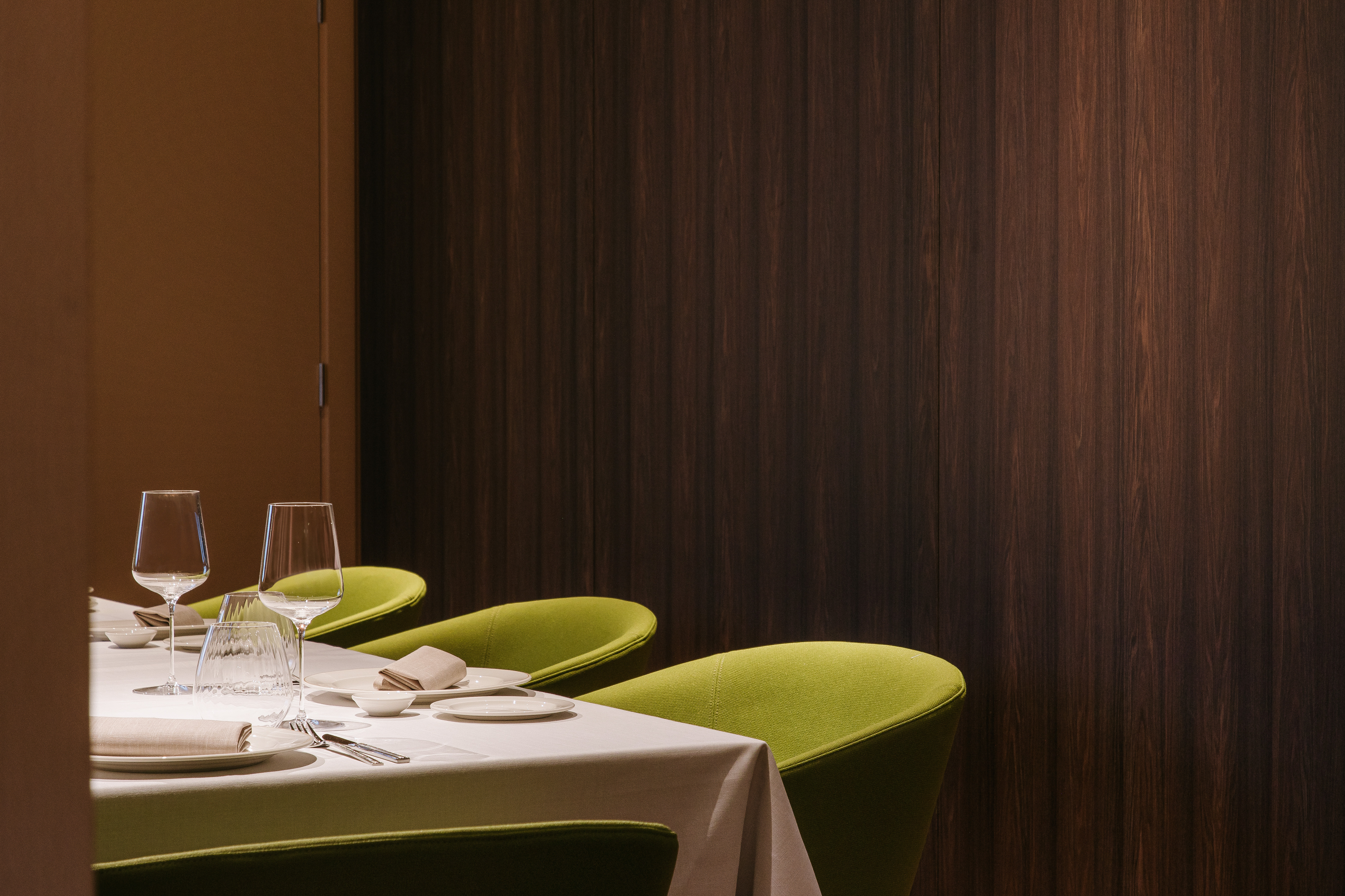 Modern restaurant interior with set table, green chairs, and wood paneling.