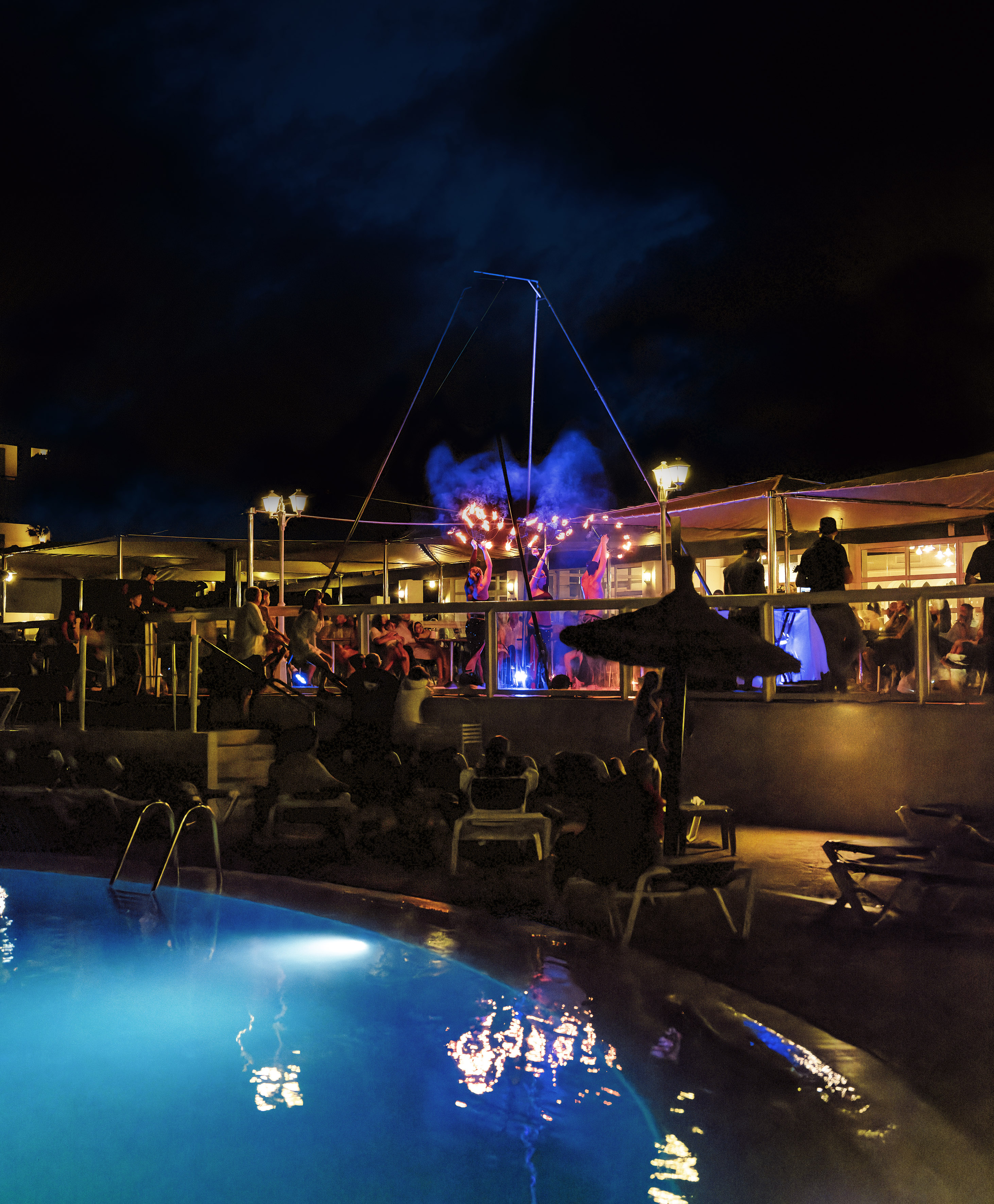 Night fire show with performers near an illuminated pool at a resort.