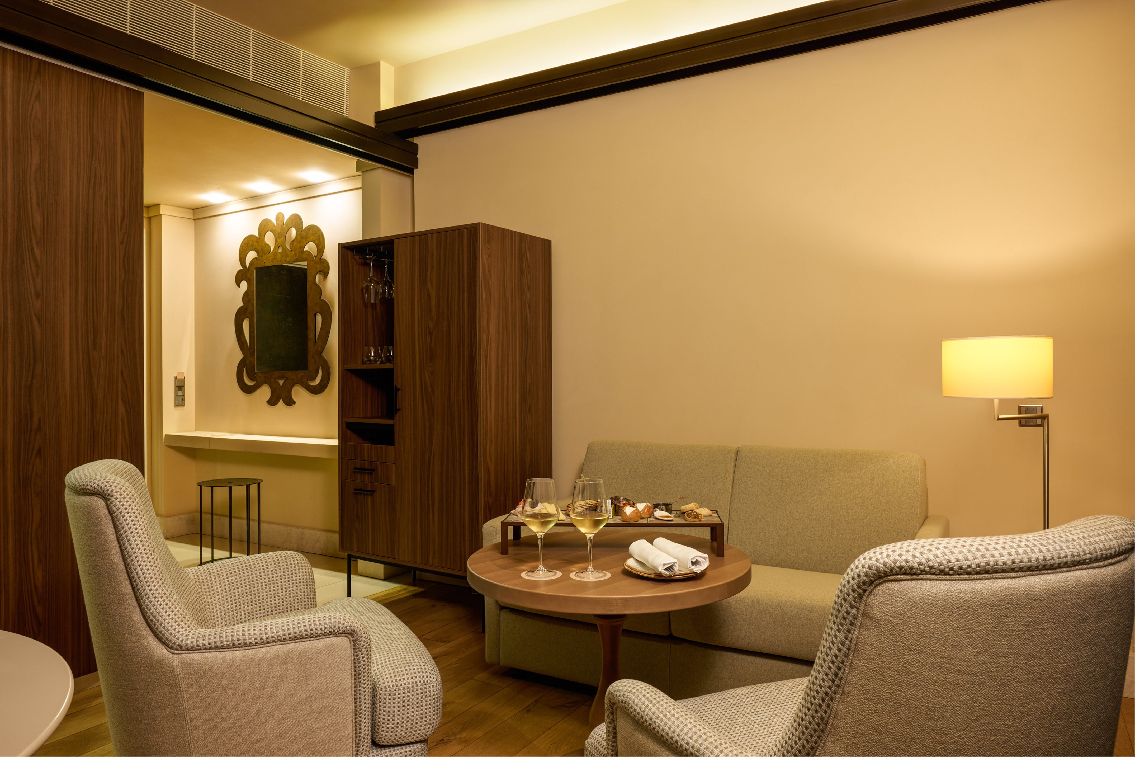 Modern hotel living room with wine, snacks, and elegant armchairs.