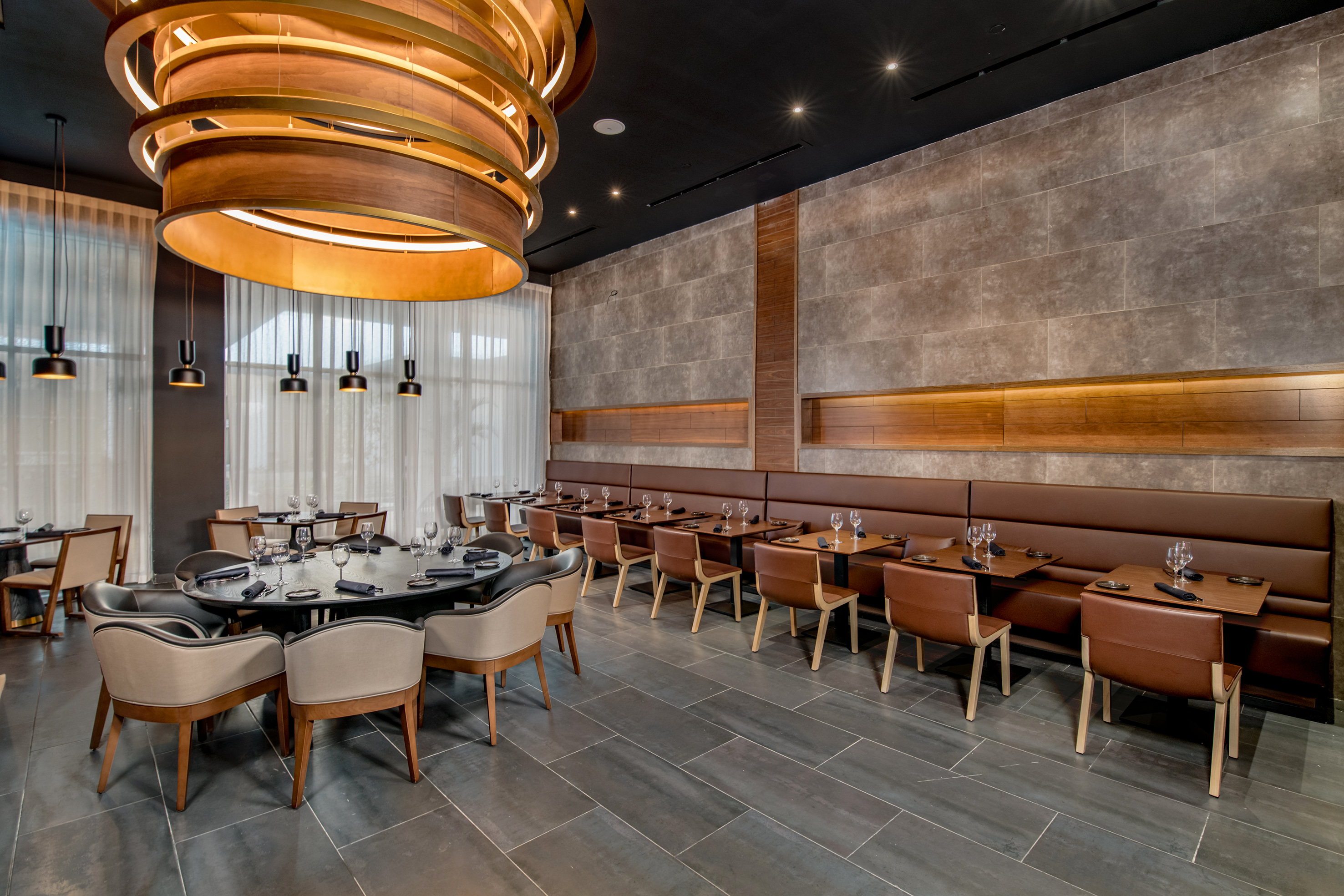 Restaurant interior: modern wood chandelier, stone wall, brown banquette seating.