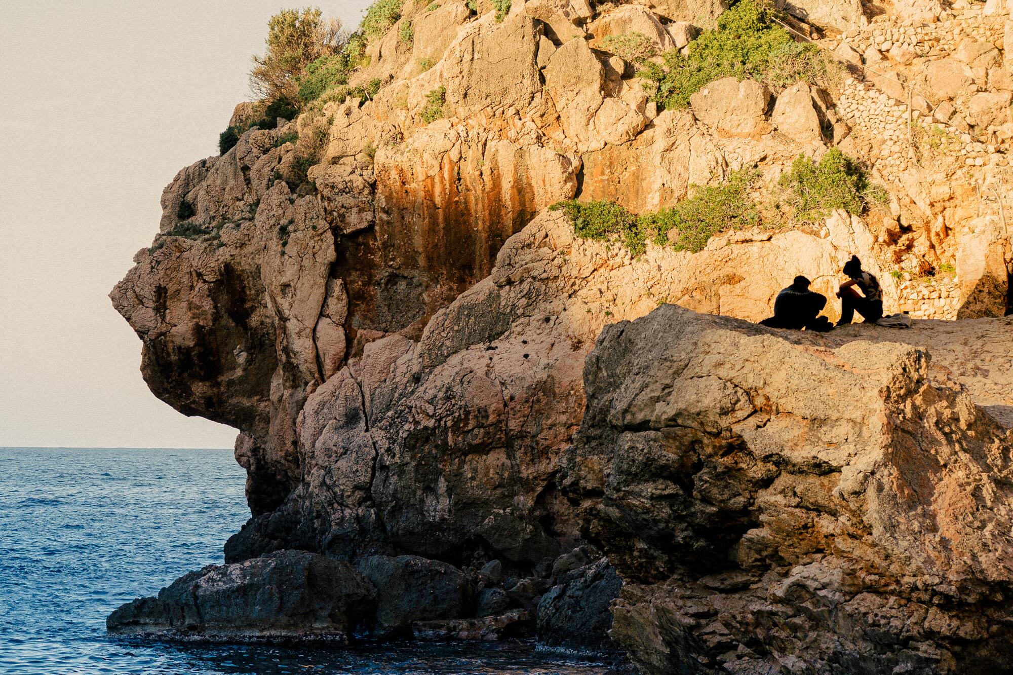 two people sitting on a cliff above the water