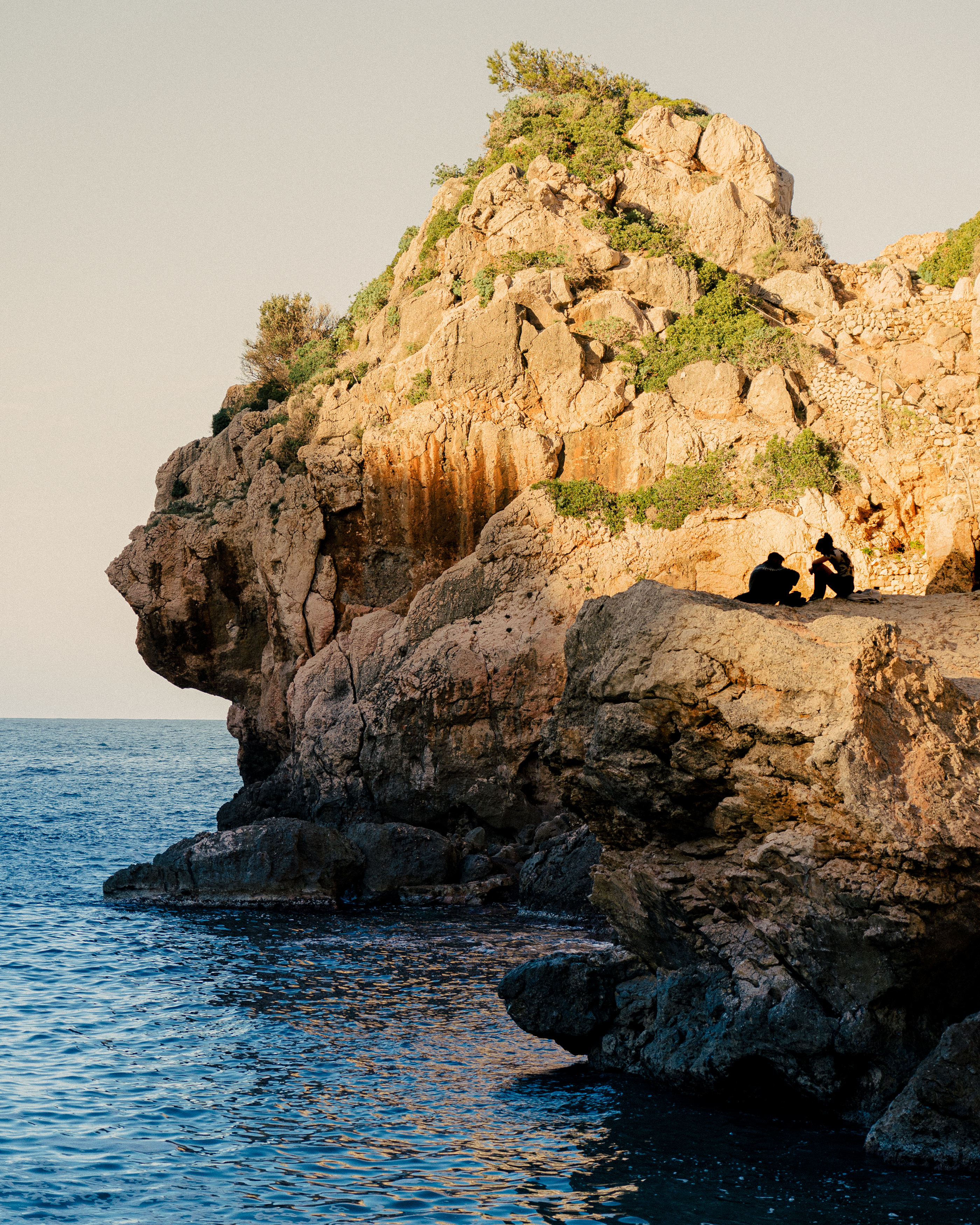 two people sitting on a cliff above the water