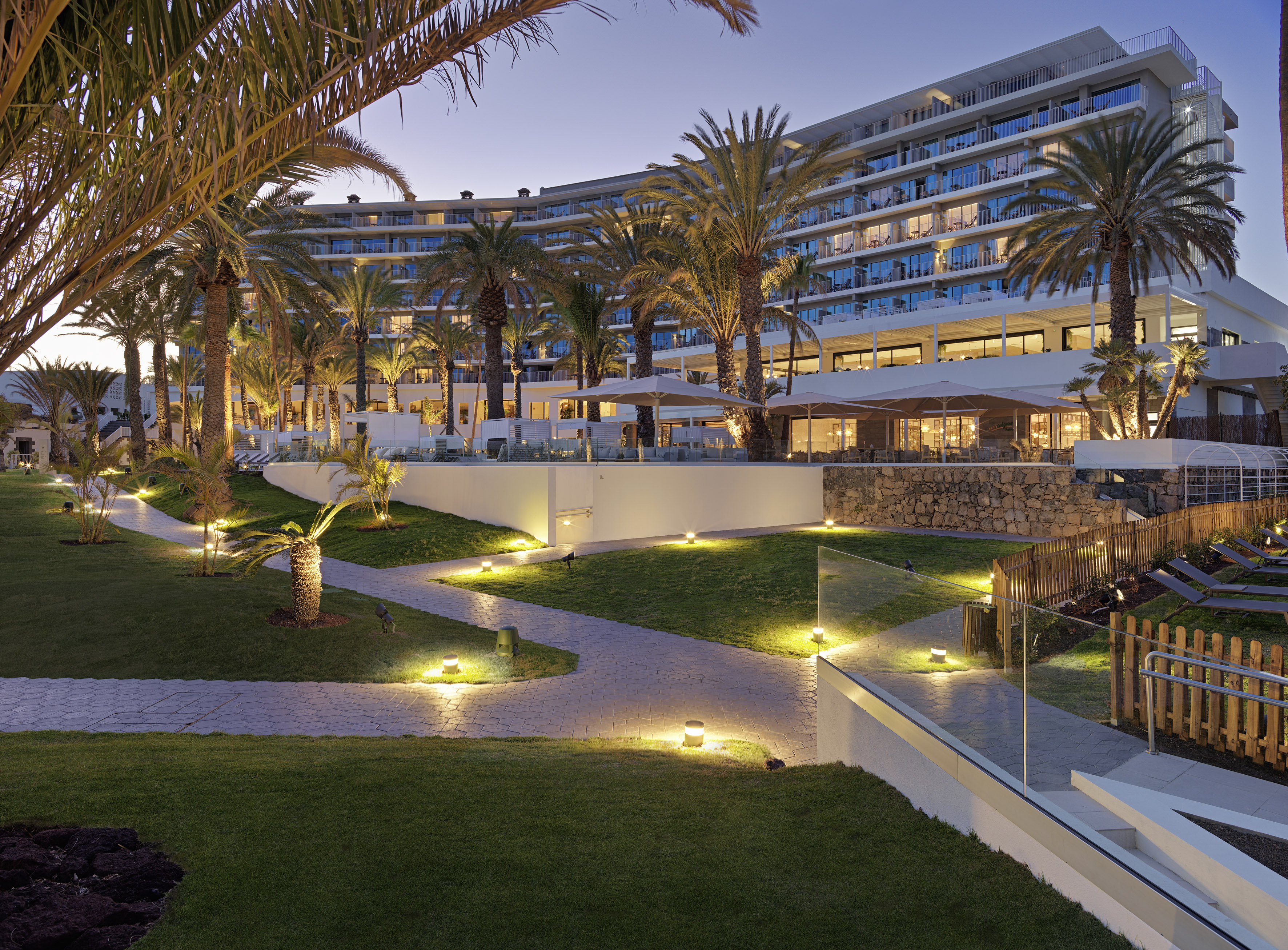 Illuminated tropical resort hotel with palm trees and landscaped gardens at dusk.