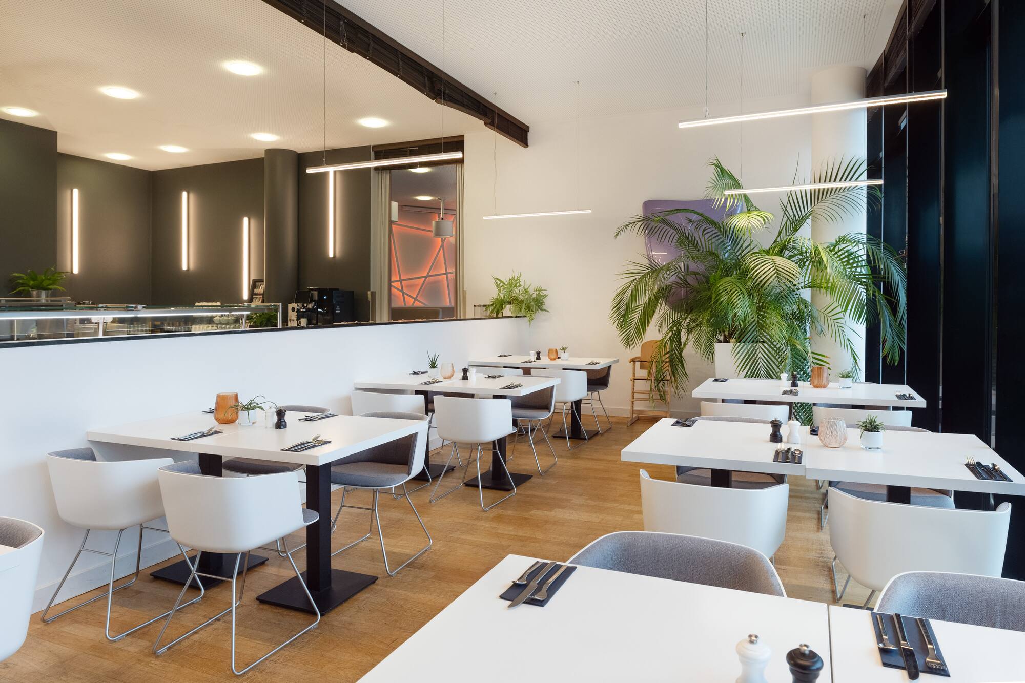 Modern restaurant interior with white tables, wooden floor, and green plants.