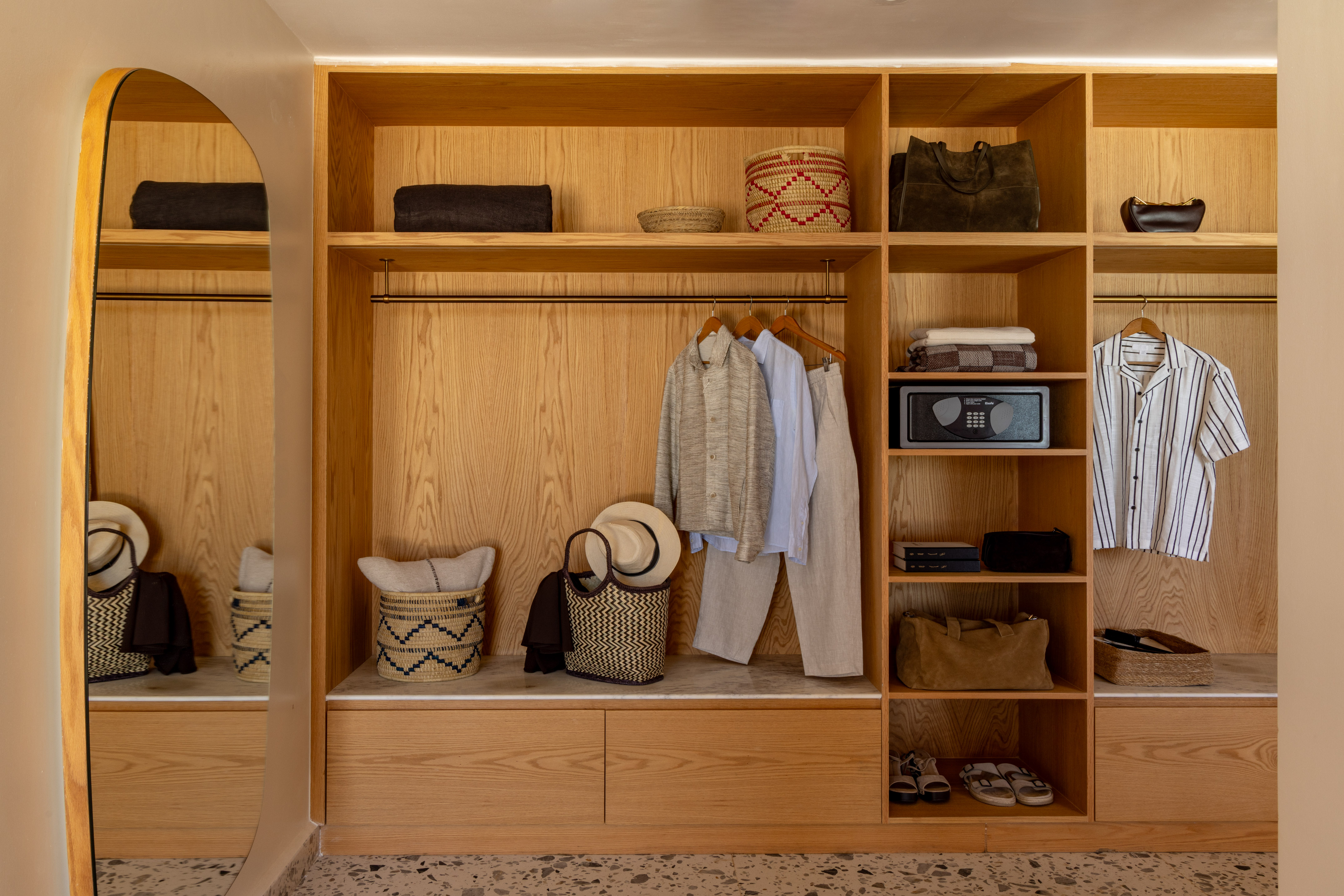 Built-in wooden wardrobe with hanging clothes, storage baskets, safe, and mirror.