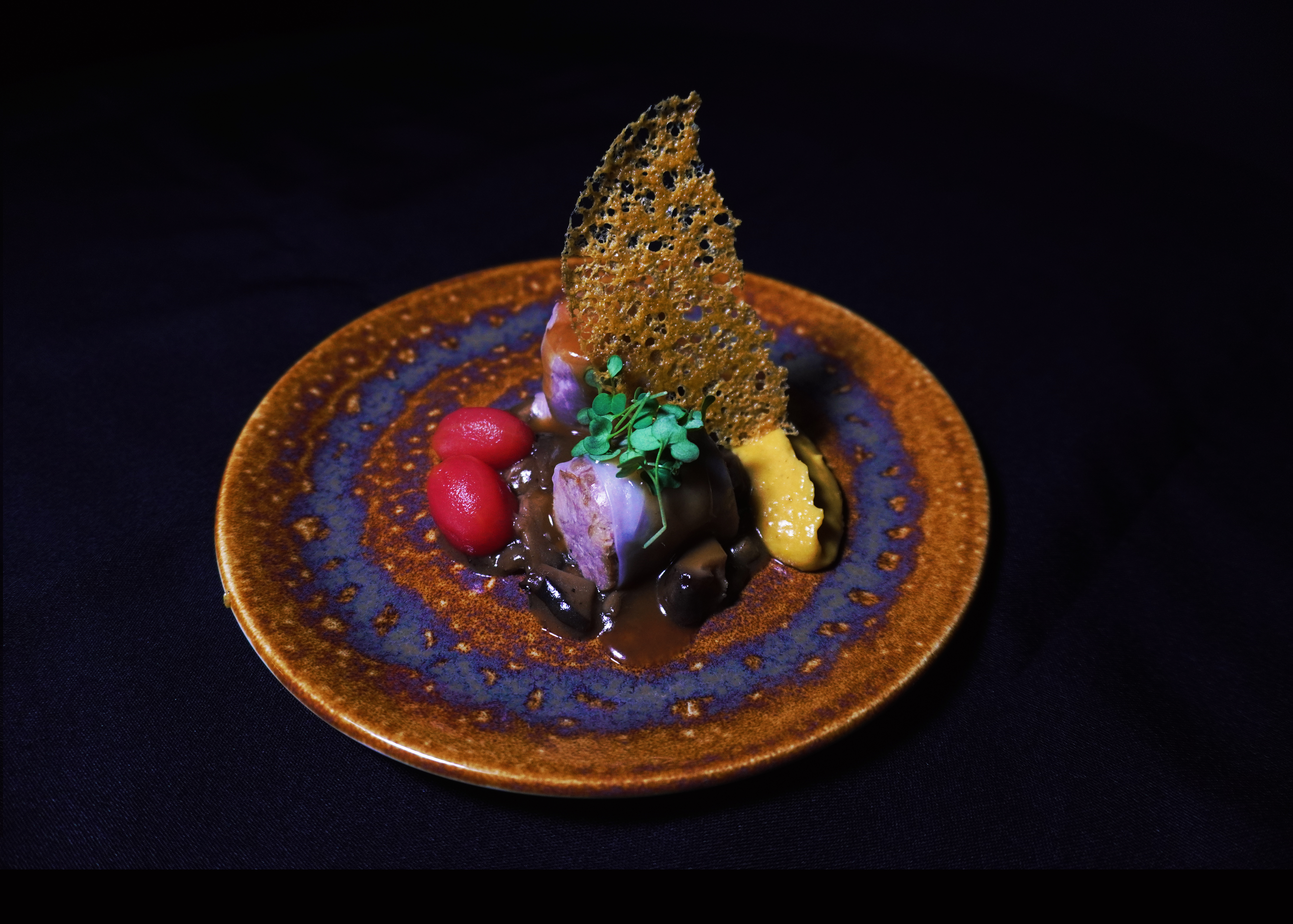 Gourmet plated dish with purple main, red berries, microgreens, and crisp tuile.