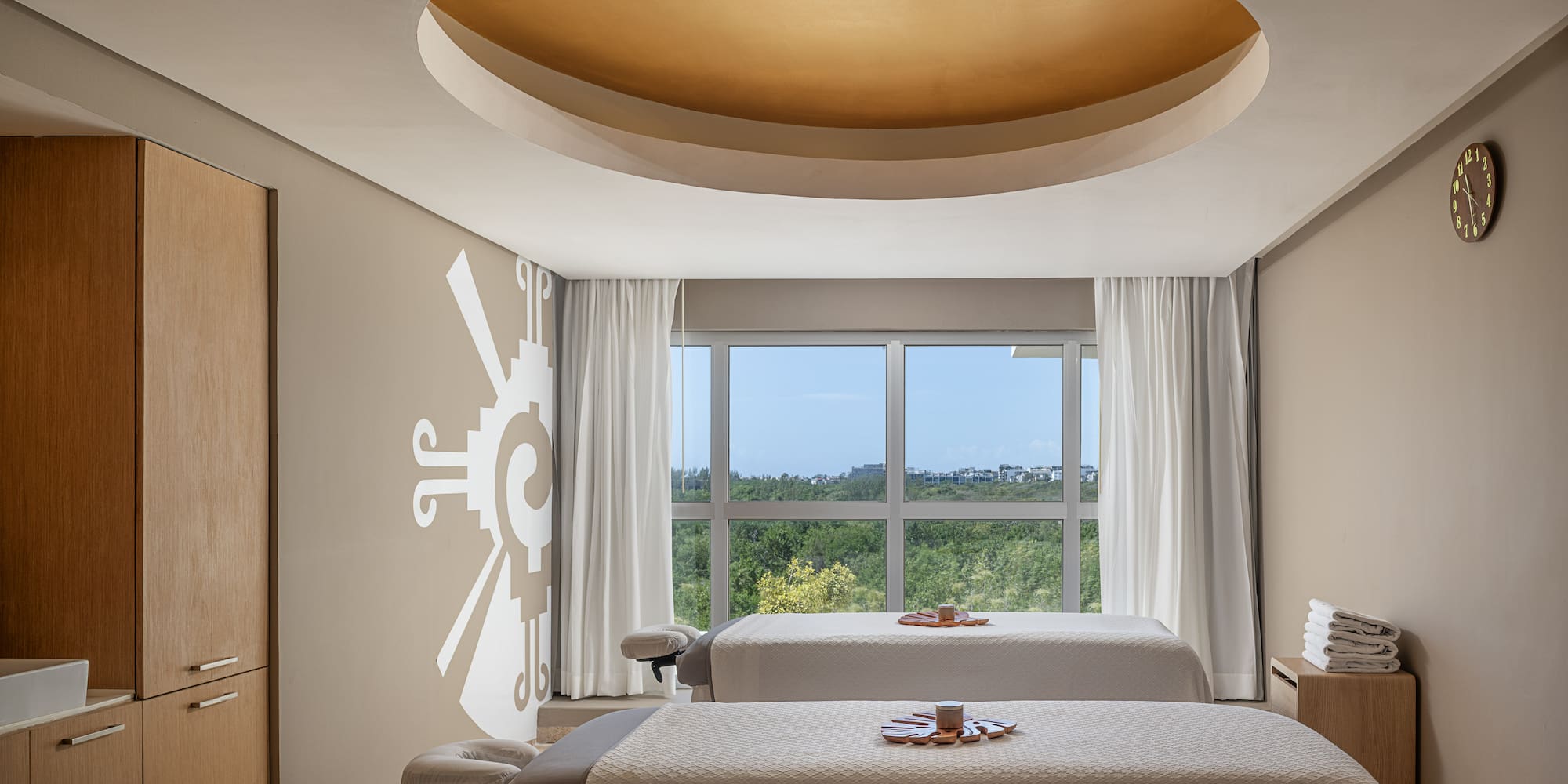 Upscale spa treatment room with two massage tables, window view, and golden ceiling.