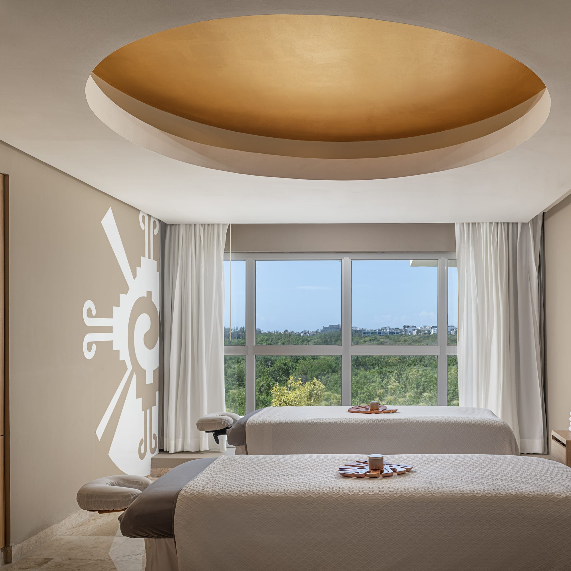 Upscale spa treatment room with two massage tables, window view, and golden ceiling.