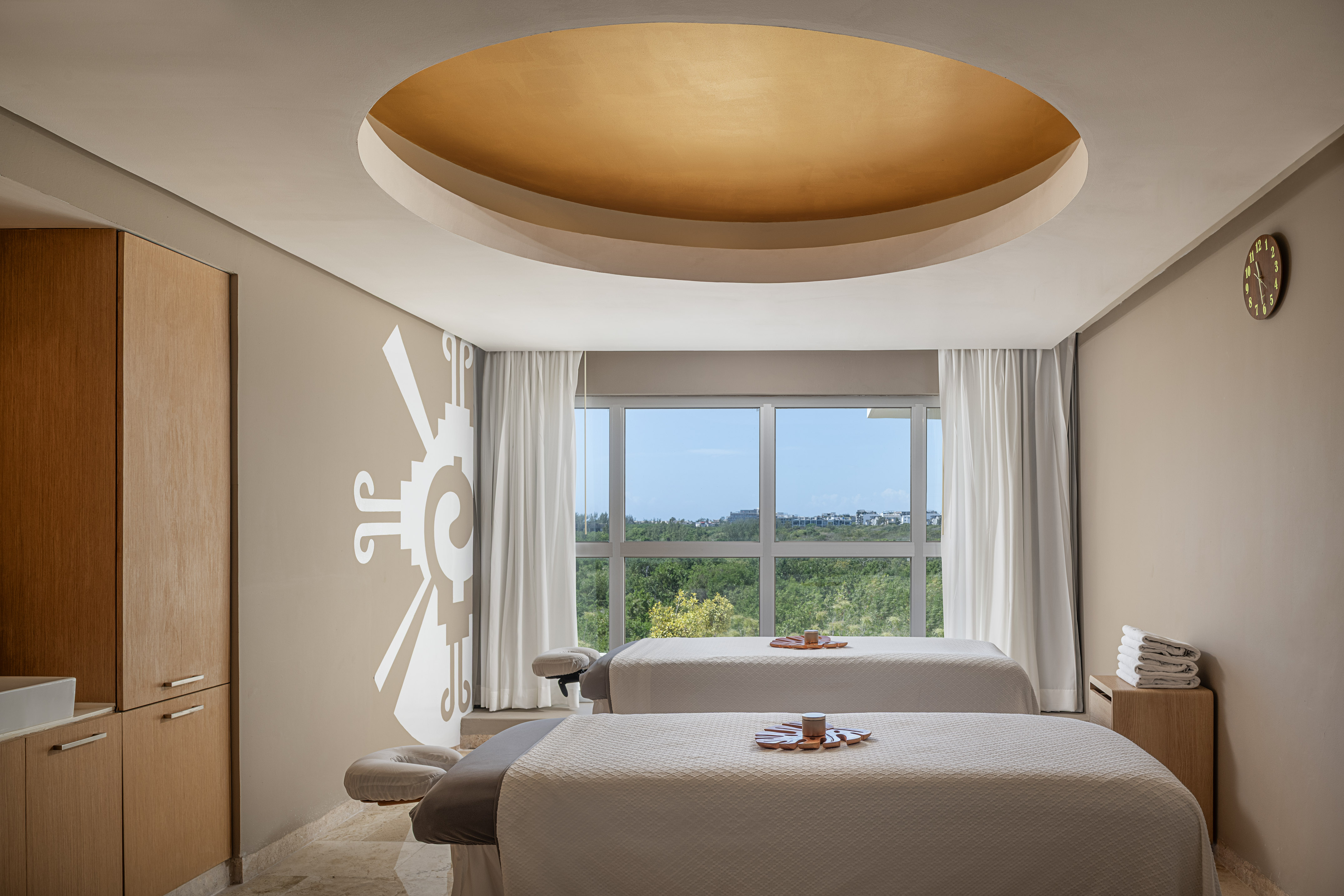 Upscale spa treatment room with two massage tables, window view, and golden ceiling.