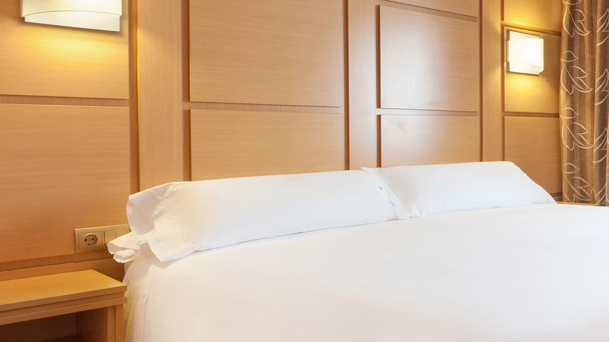 Modern hotel bedroom: white bed, wooden headboard with lit sconces.