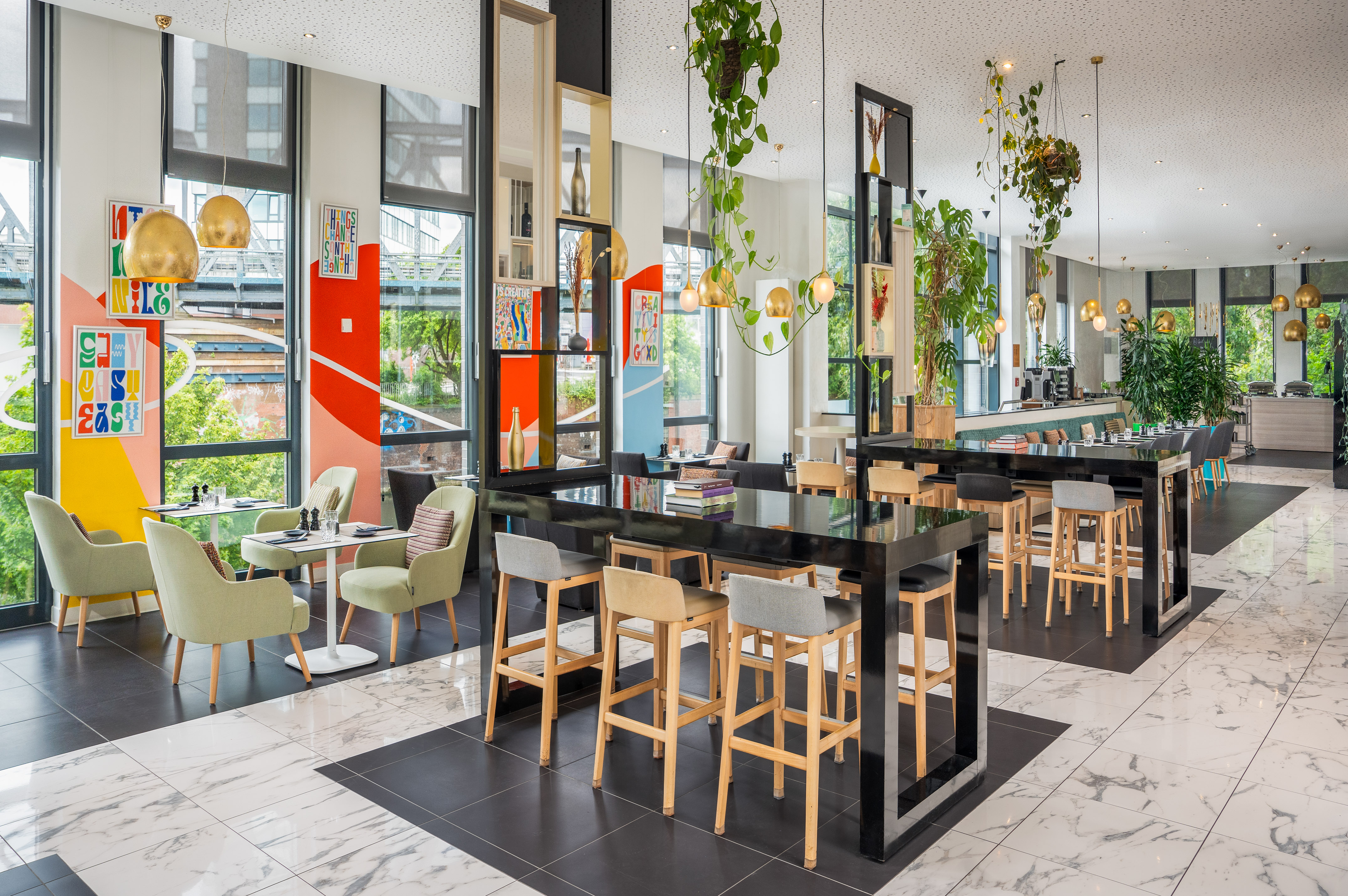Modern restaurant lounge with bar stools, green chairs, plants, and colorful walls.