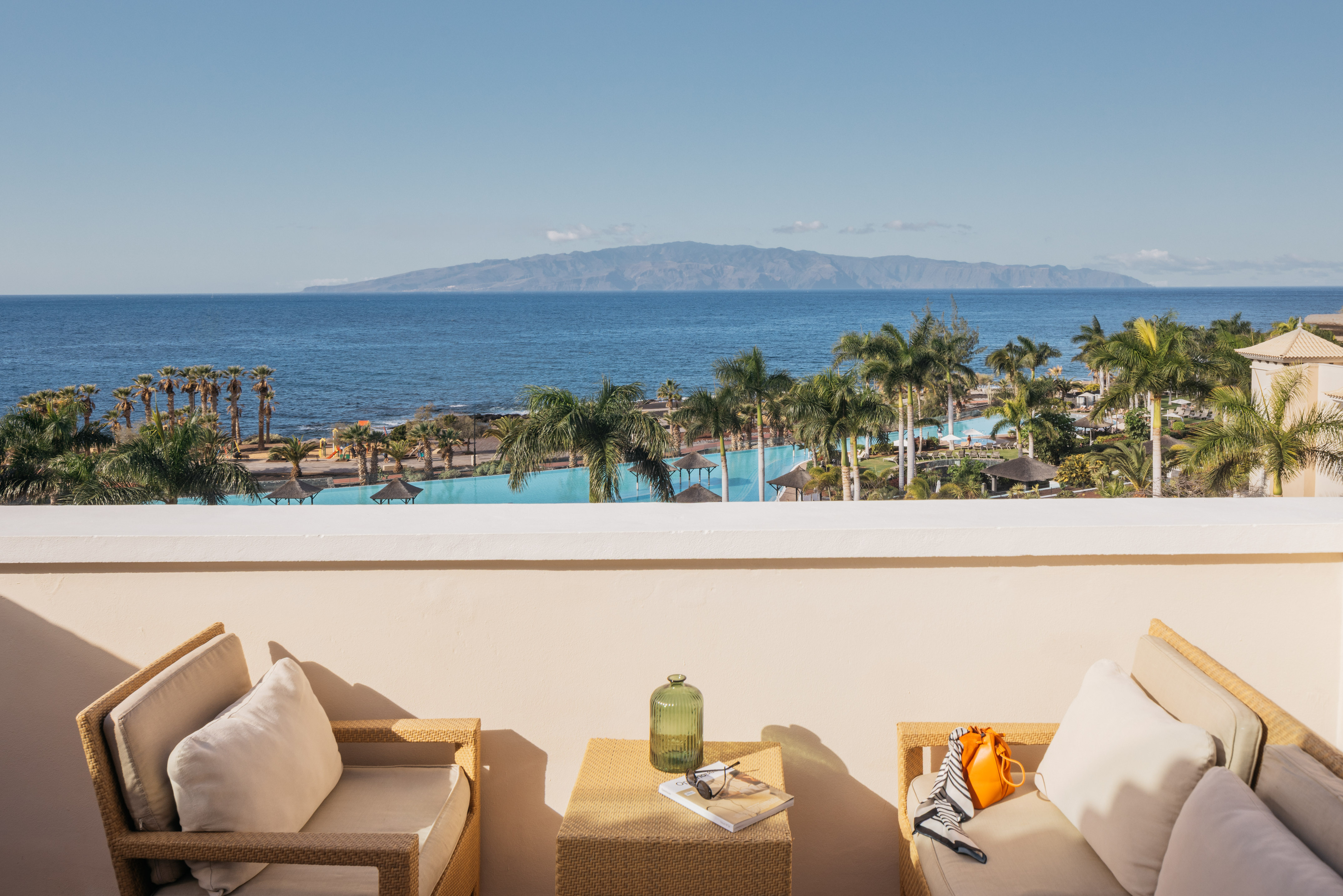 Balcony overlooking tropical ocean, resort pool, palm trees, and island view.