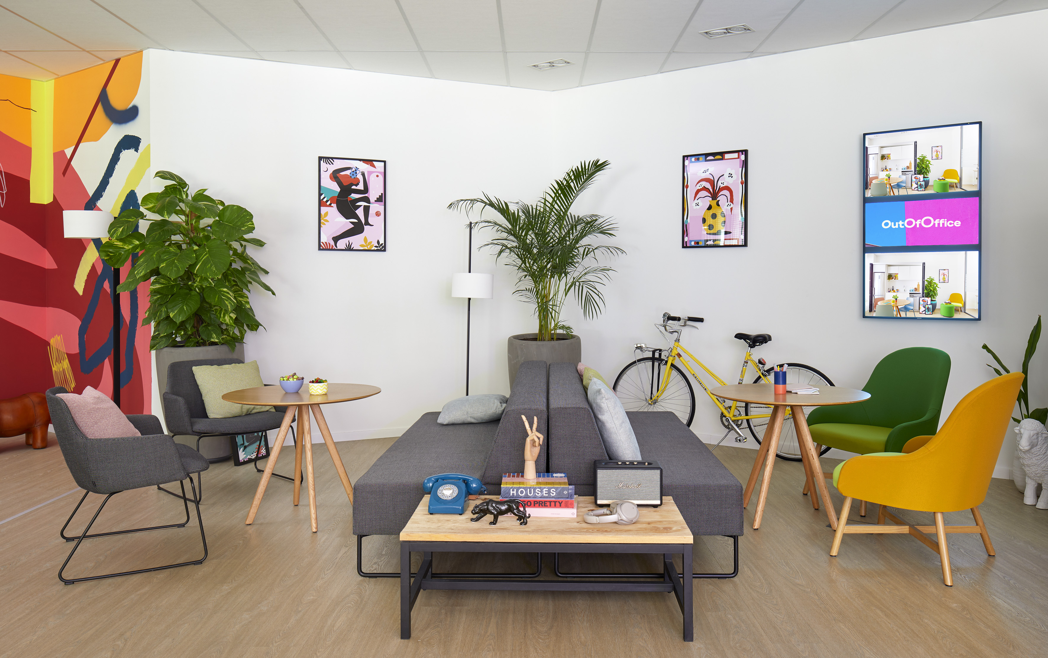 Colorful office lounge with modular sofa, vibrant art, plants, and yellow bicycle.