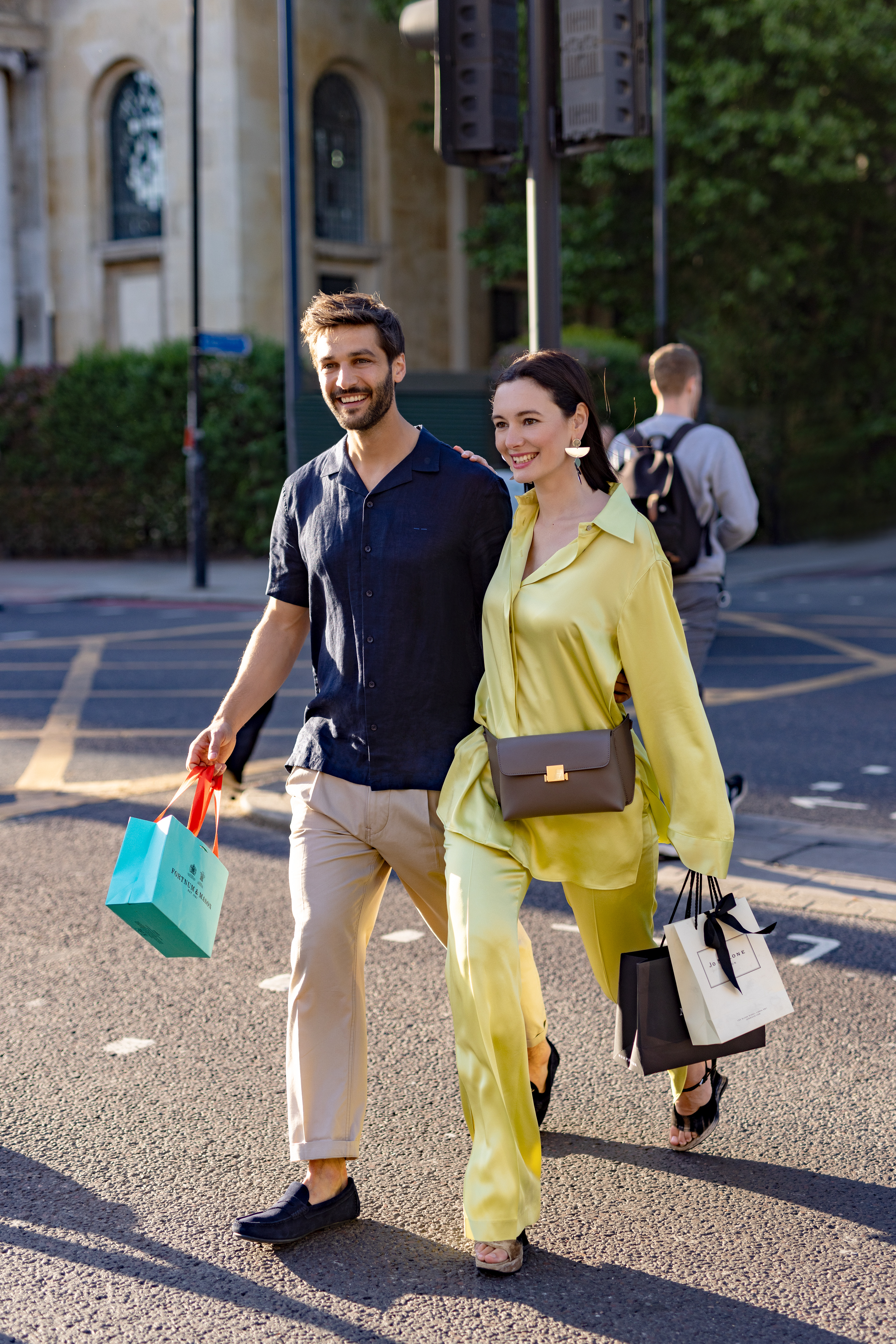 A man and a woman stroll along the street, each carrying shopping bags.