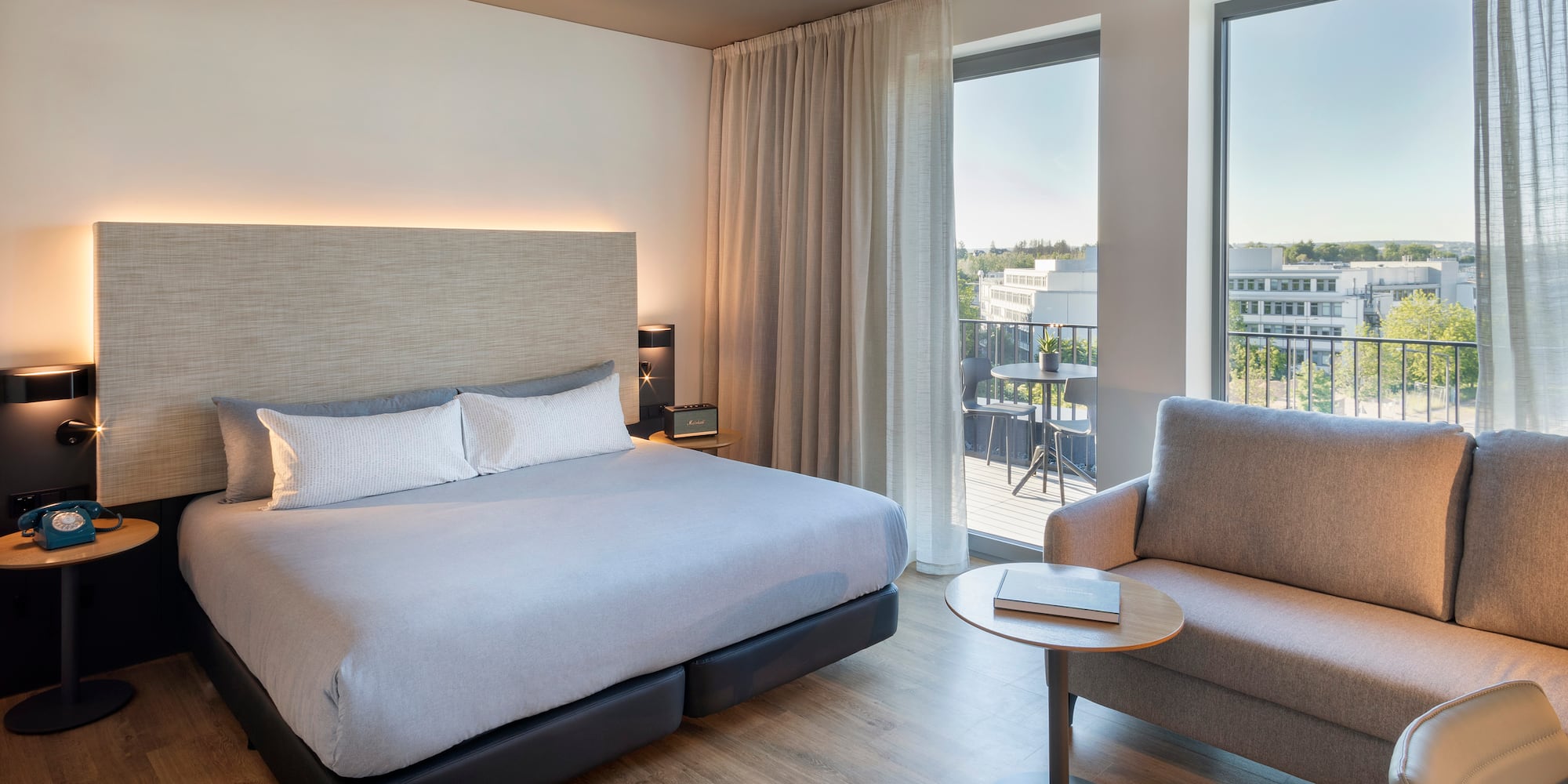 Modern hotel room with king bed, balcony access, sofa, and city view.