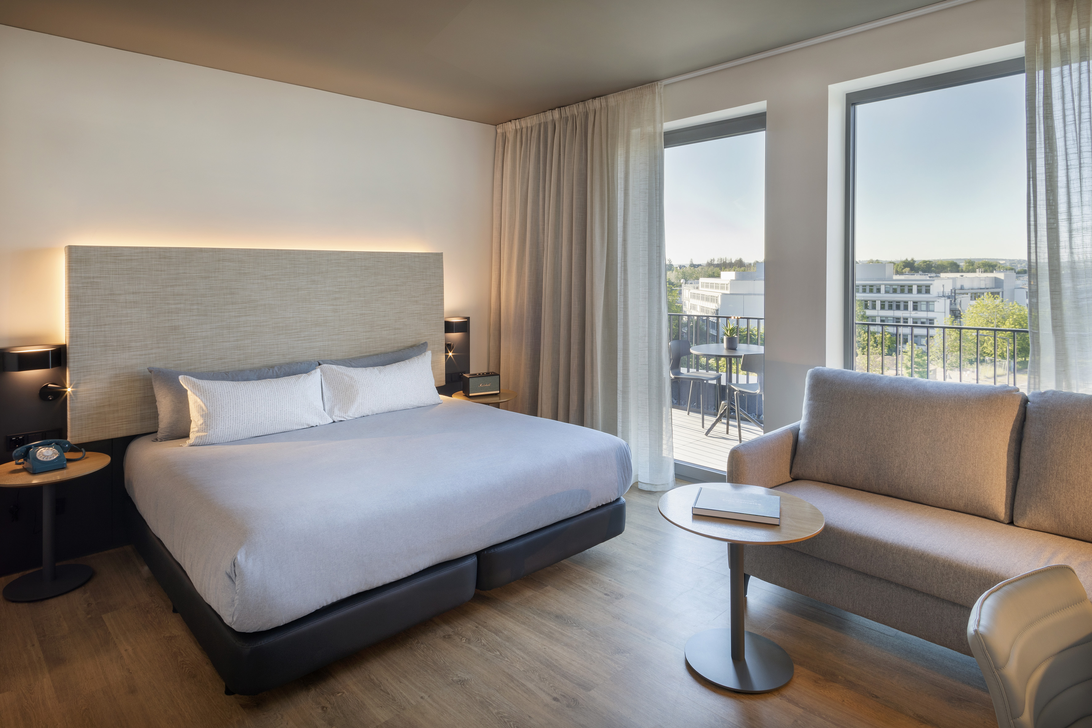 Modern hotel room with king bed, balcony access, sofa, and city view.