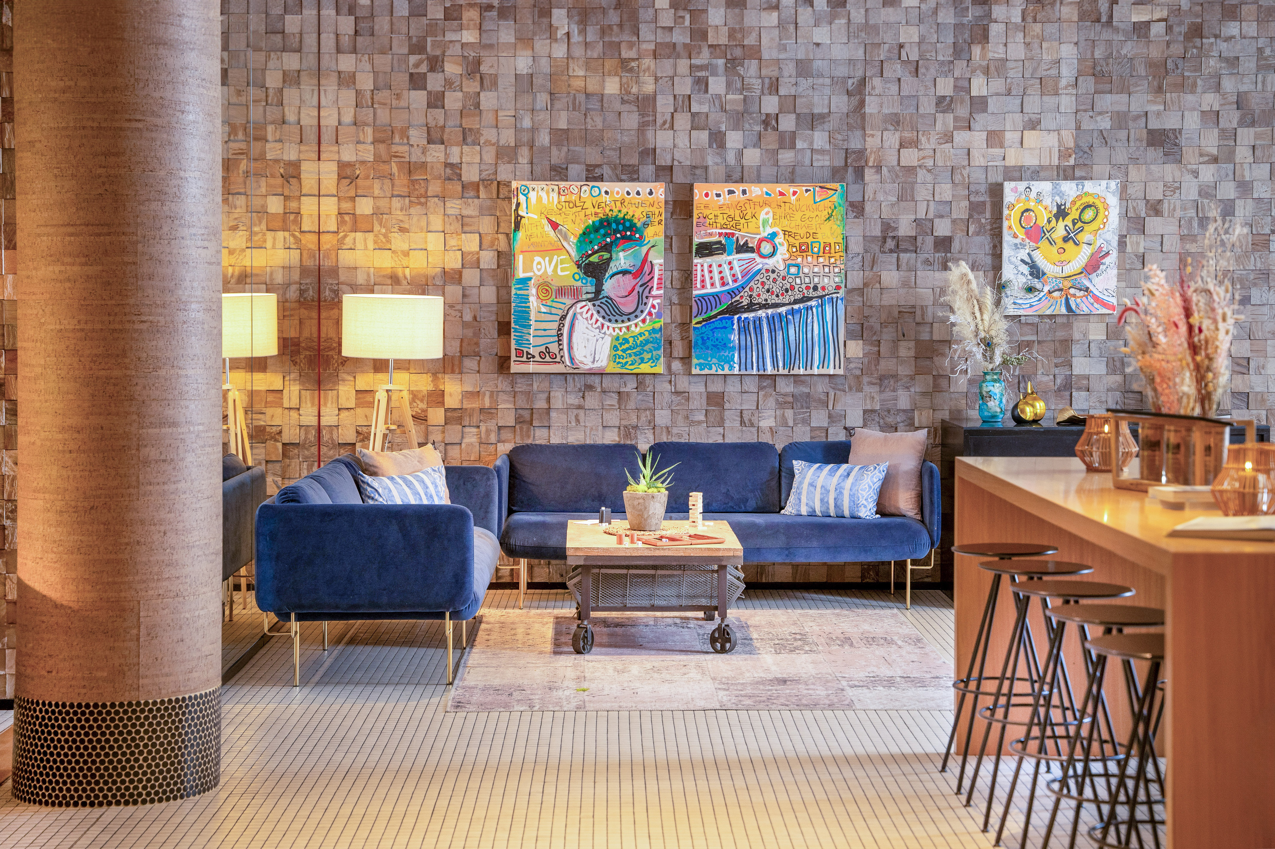 Modern hotel lobby with blue velvet sofas, wood block wall, abstract art.