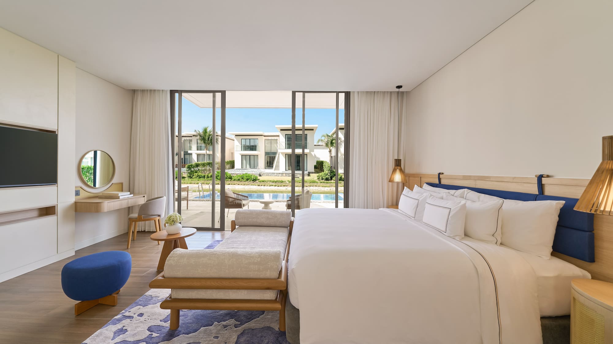 Luxury modern bedroom with king bed, blue accents, and waterfront villa view.