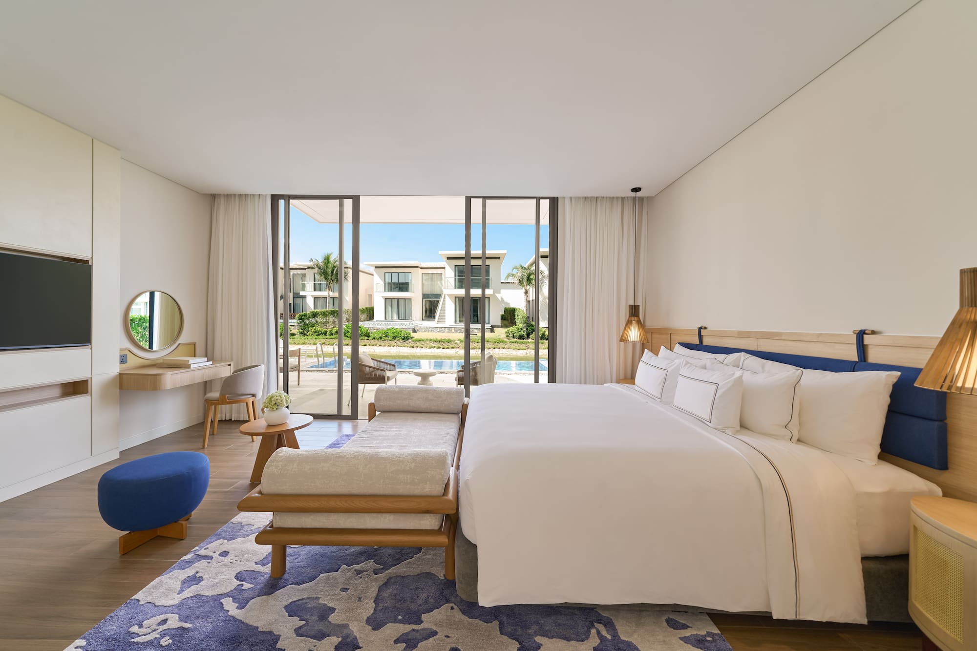Luxury modern bedroom with king bed, blue accents, and waterfront villa view.