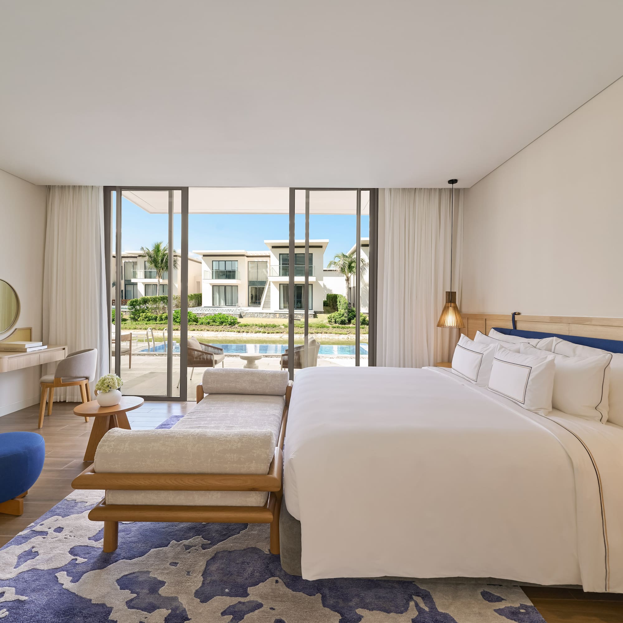 Luxury modern bedroom with king bed, blue accents, and waterfront villa view.