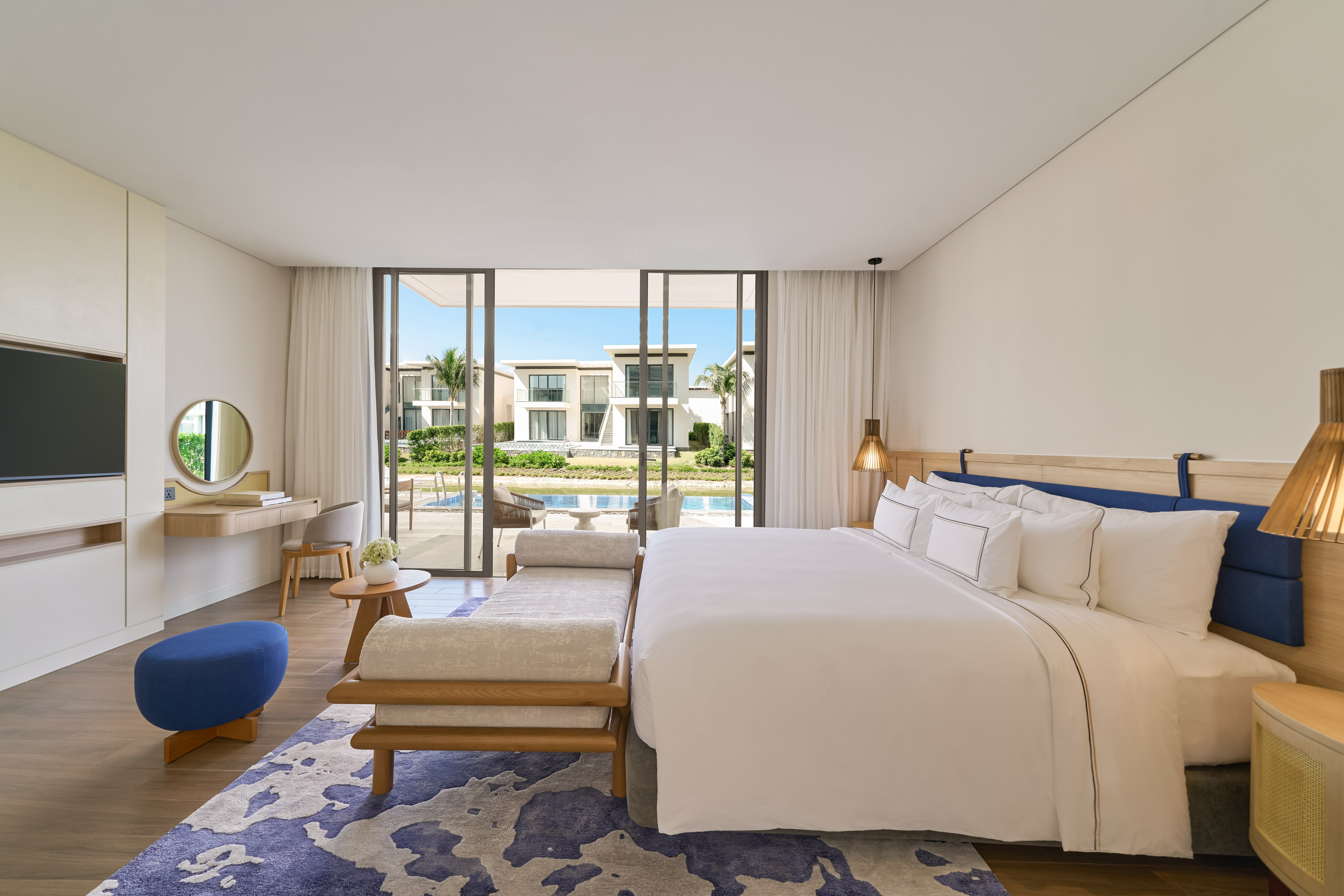 Luxury modern bedroom with king bed, blue accents, and waterfront villa view.